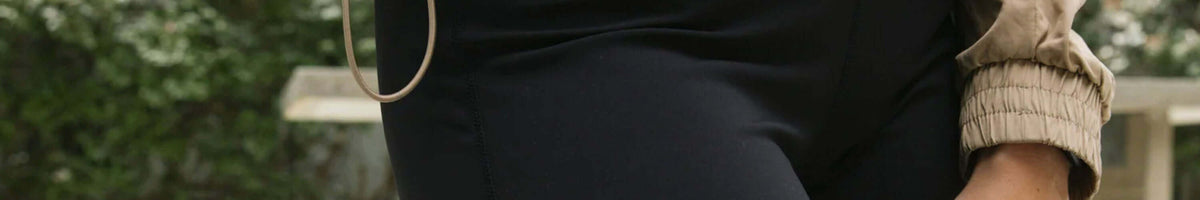 Marlow black travel pants and beige knit sleeve worn outdoors, close-up brand banner
