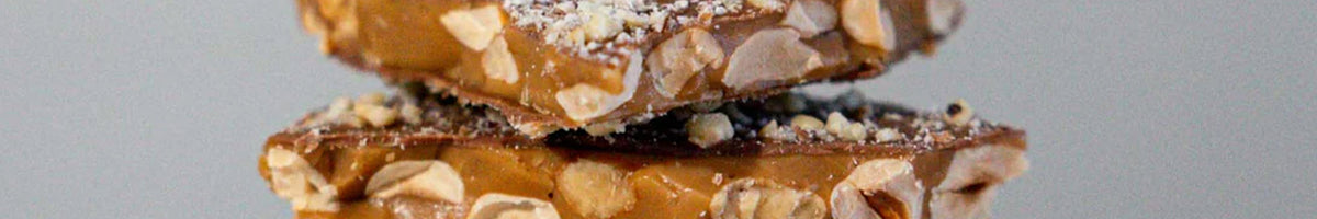 The Confectionist toffee brittle slabs with roasted nuts stacked, close-up brand banner