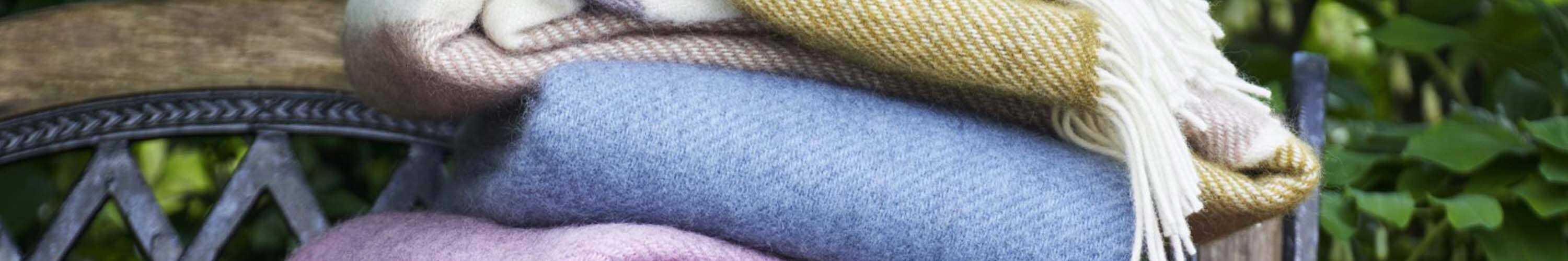 Stack of colorful Klippan Yllefabrik woollen blankets on a rustic chair.