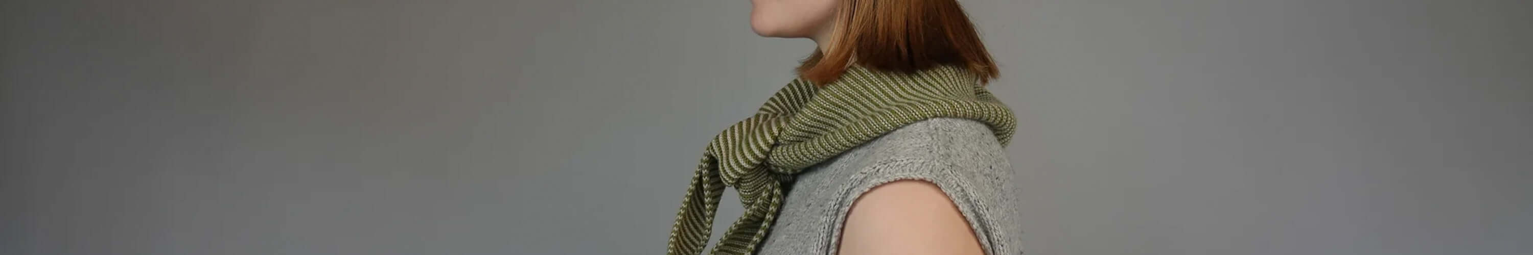 Profile view of a woman wearing a stylish green scarf and a grey vest from the Knit Shepherd collection.