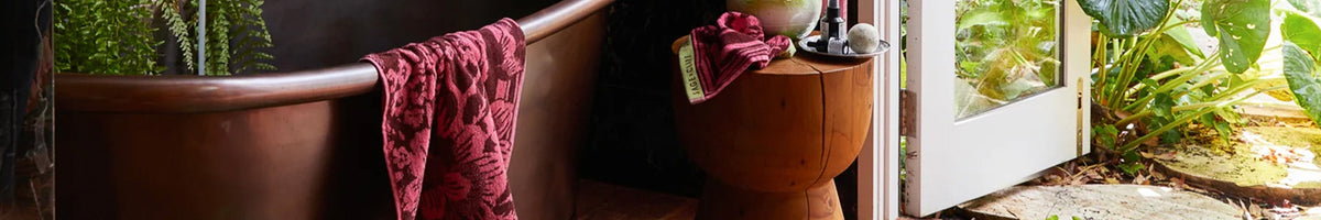 Sage x Clare vibrant Australian homewares scene with bold patterned towels, wooden tub, and sunlit indoor plants