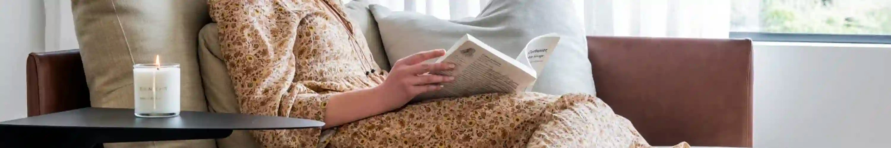 Alt Tag: Lyttelton Lights soy candle on side table beside woman reading on sofa in sunlit living room, luxury home fragrance NZ
