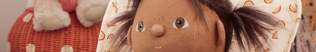 Olli Ella Dinkum doll close-up with brown hair on rainbow pillow, sustainable kids toy collection
