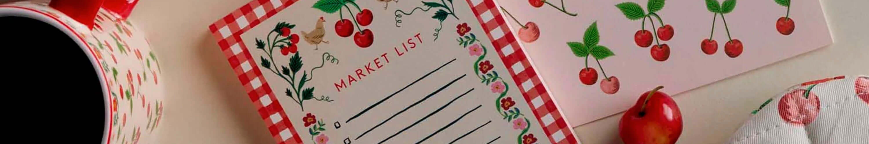 Rifle Paper cherry market list notepad with floral border and matching stationery on desk