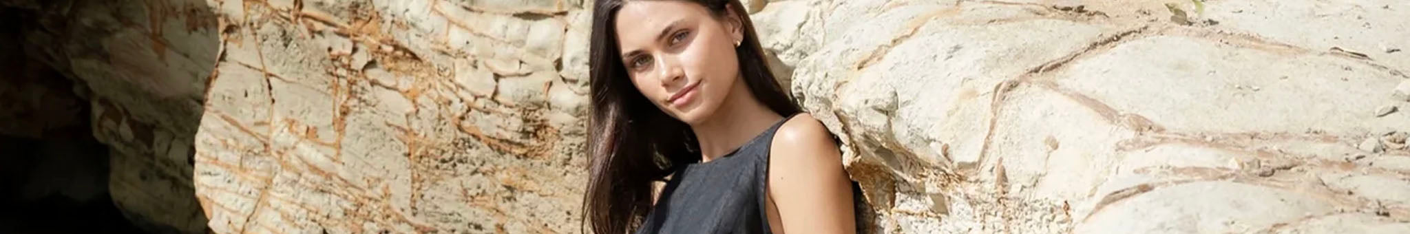 Sophie New Zealand designed capsule clothing and jewellery collection model wearing black dress by stone wall