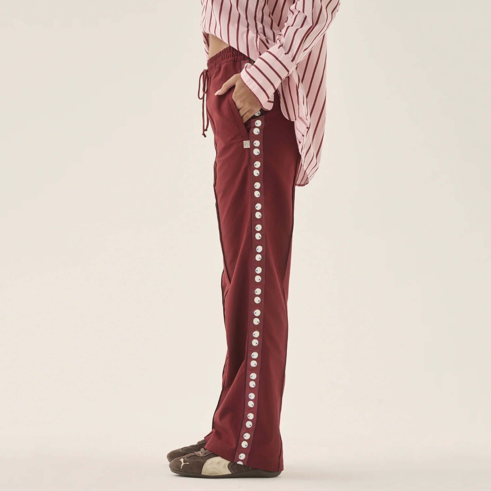Araminta James Pomodoro Twill Pants - Burgundy displayed on model, featuring snap-stud side trims and a stylish straight-leg cut.