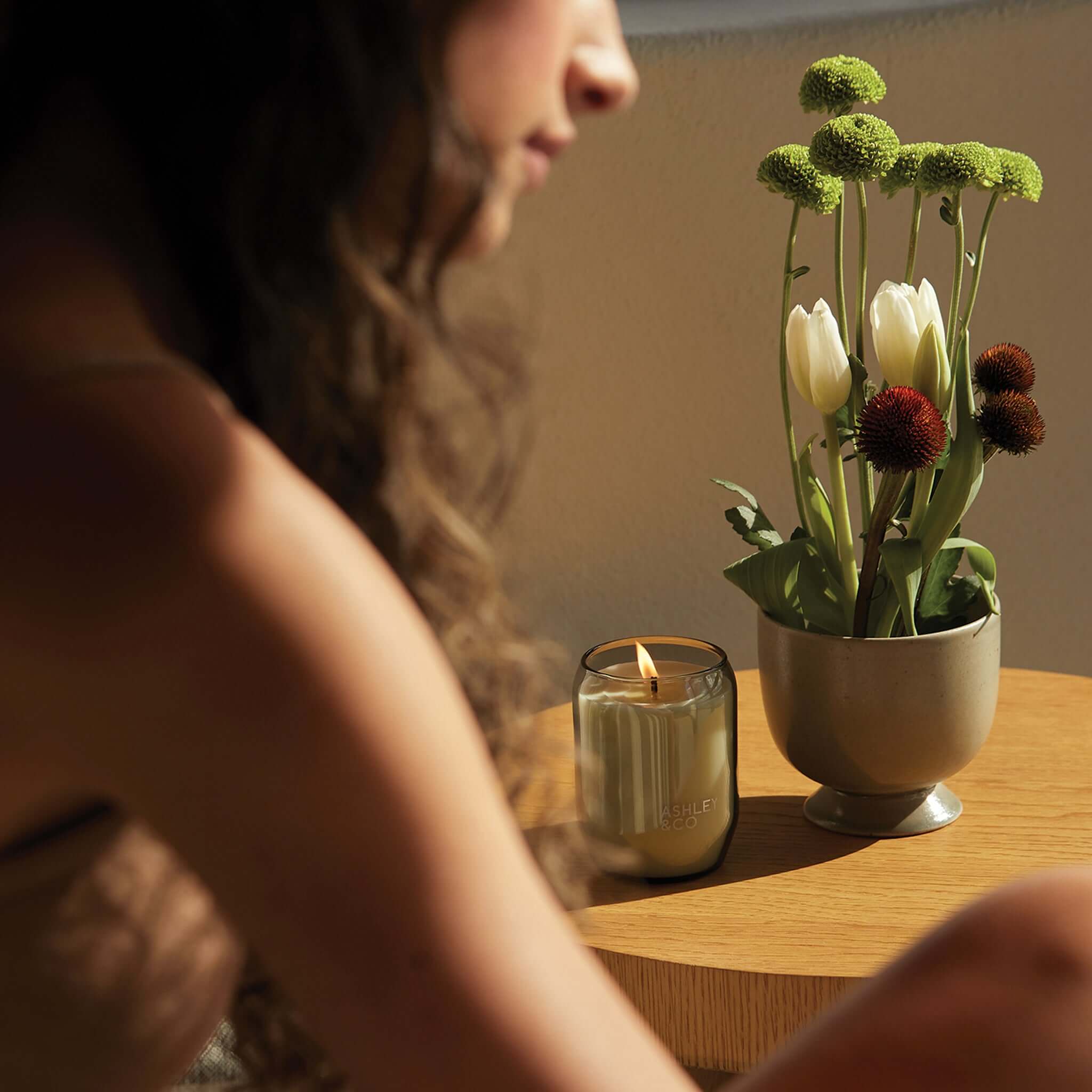 Ashley & Co Waxed Perfume Candle burning on wooden table beside vase of flowers, natural wax handmade New Zealand scented candle