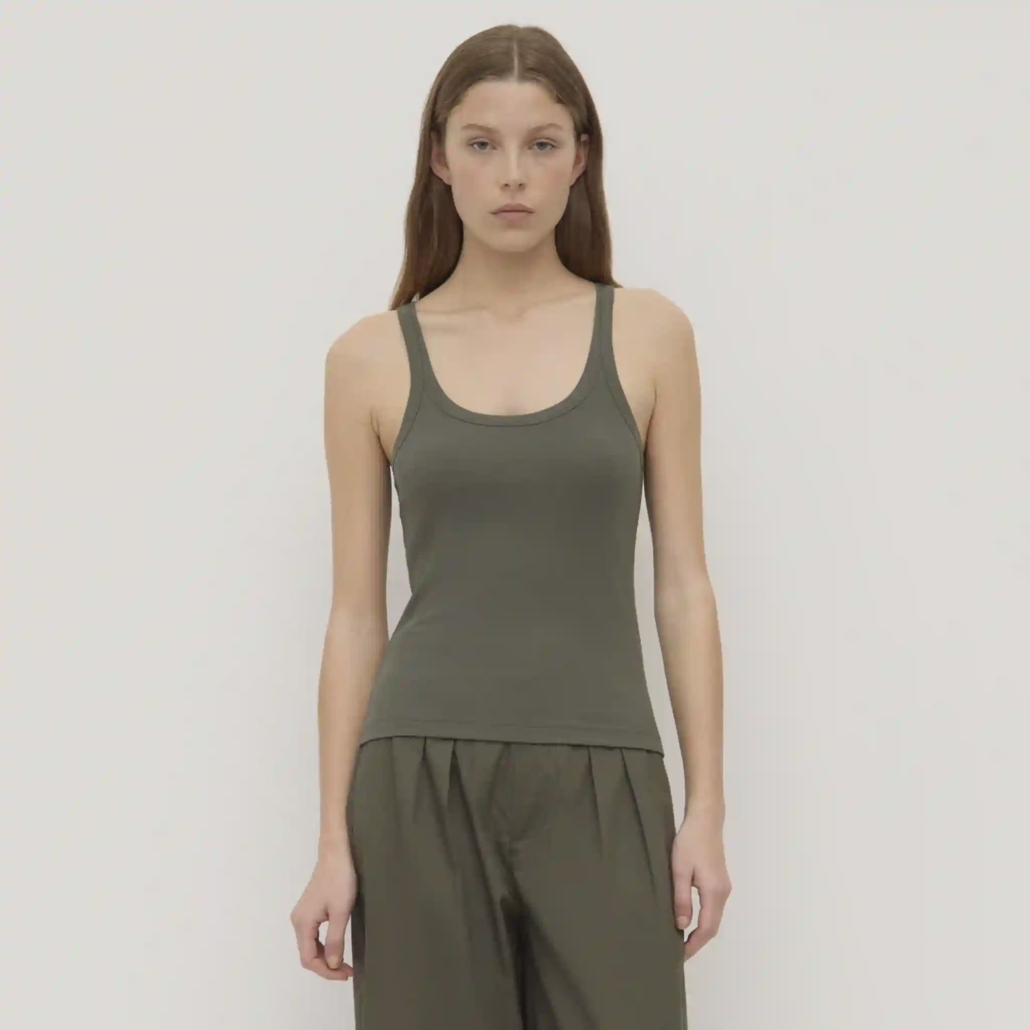 Woman wearing a green tank top and pants against a plain background