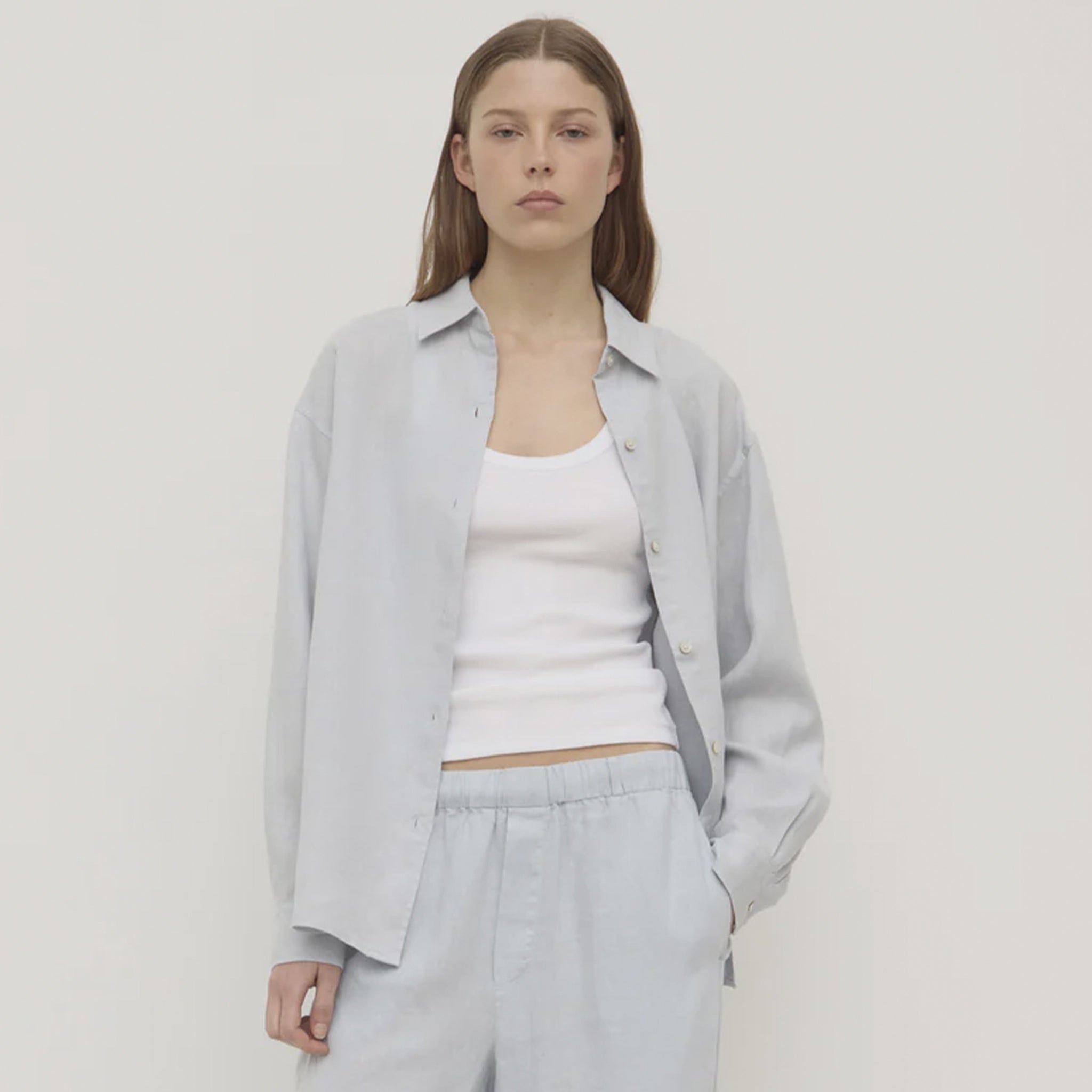 Woman wearing a light gray shirt over a white top and pants on a plain background