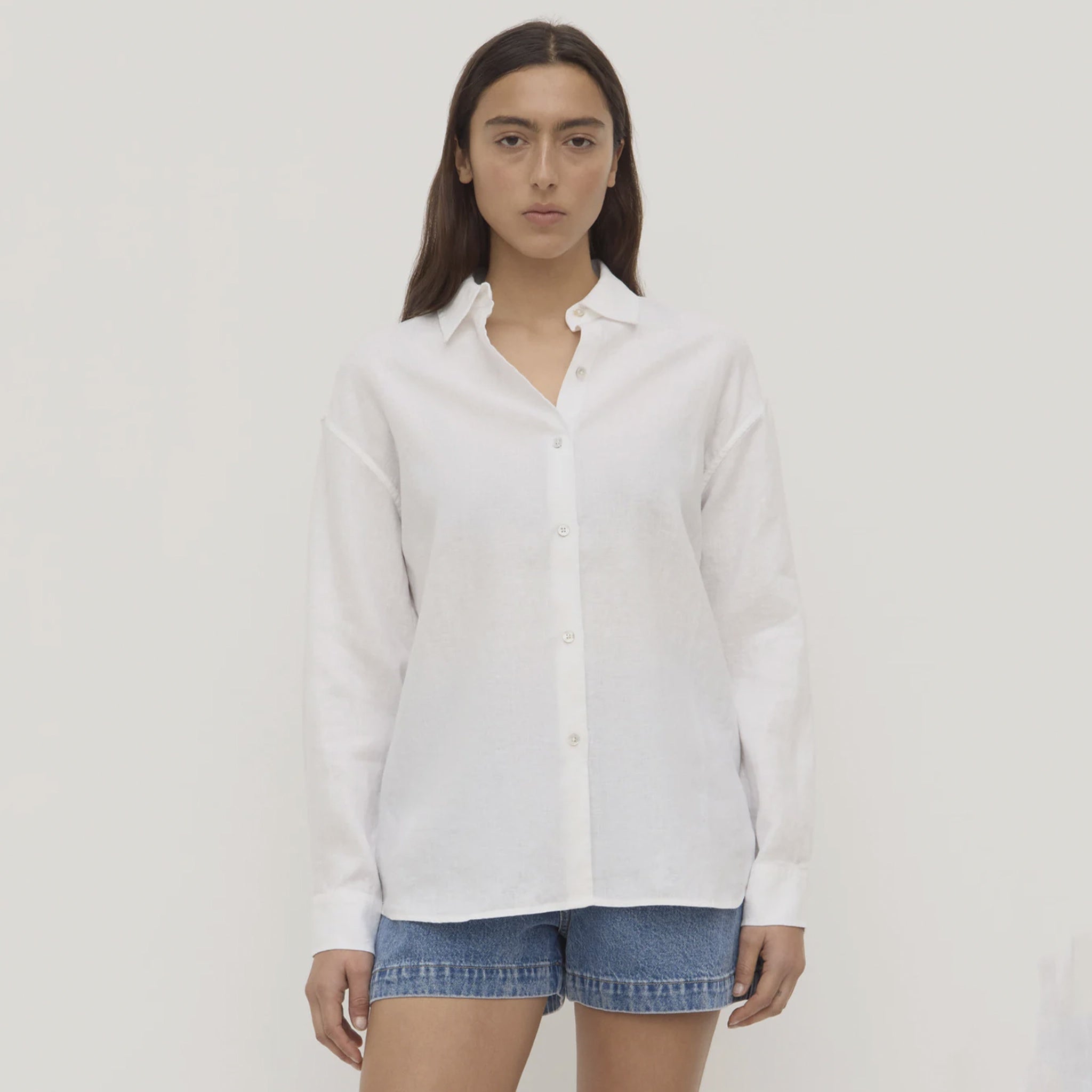 Person wearing a white shirt and denim shorts on a plain background