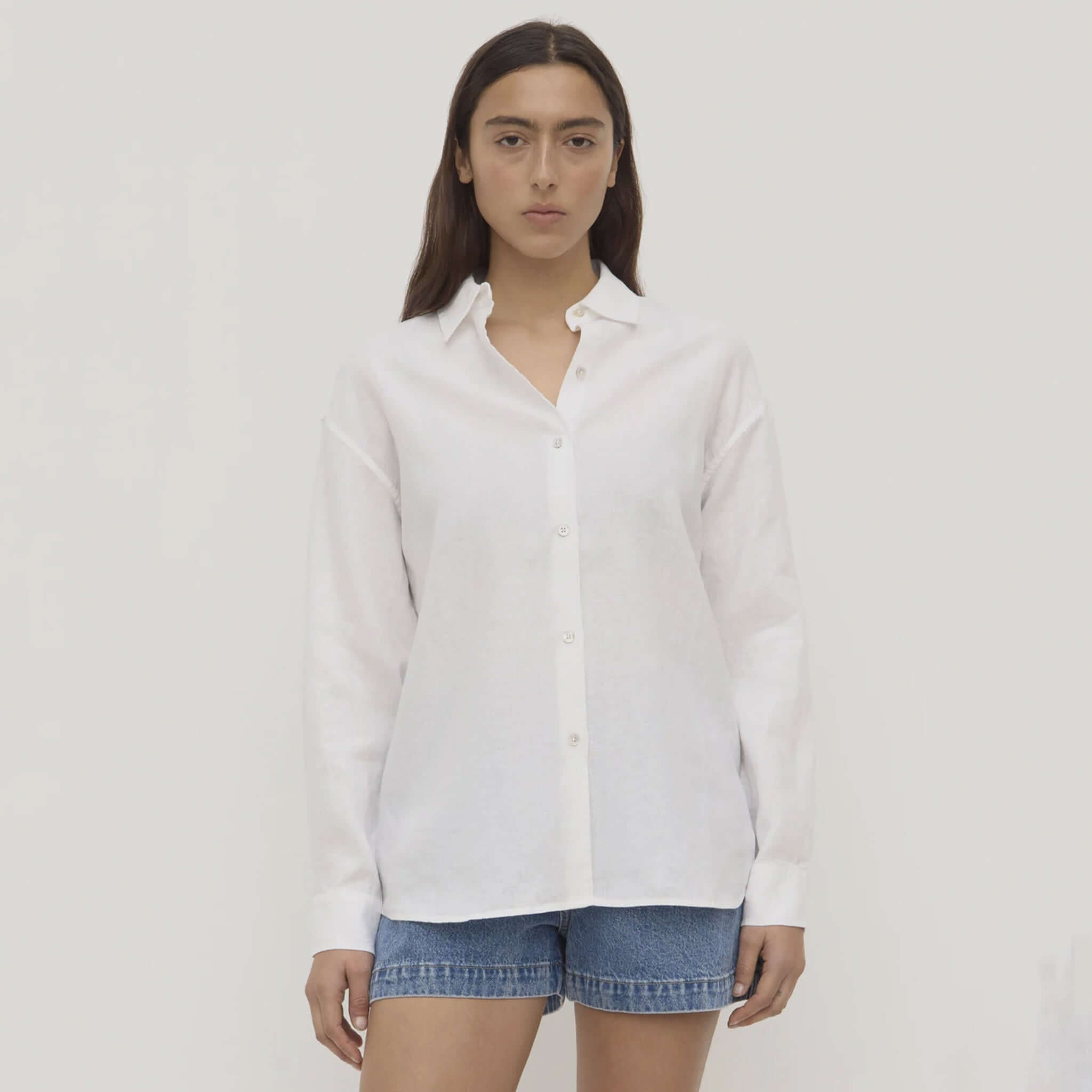 Person wearing a white shirt and denim shorts on a plain background