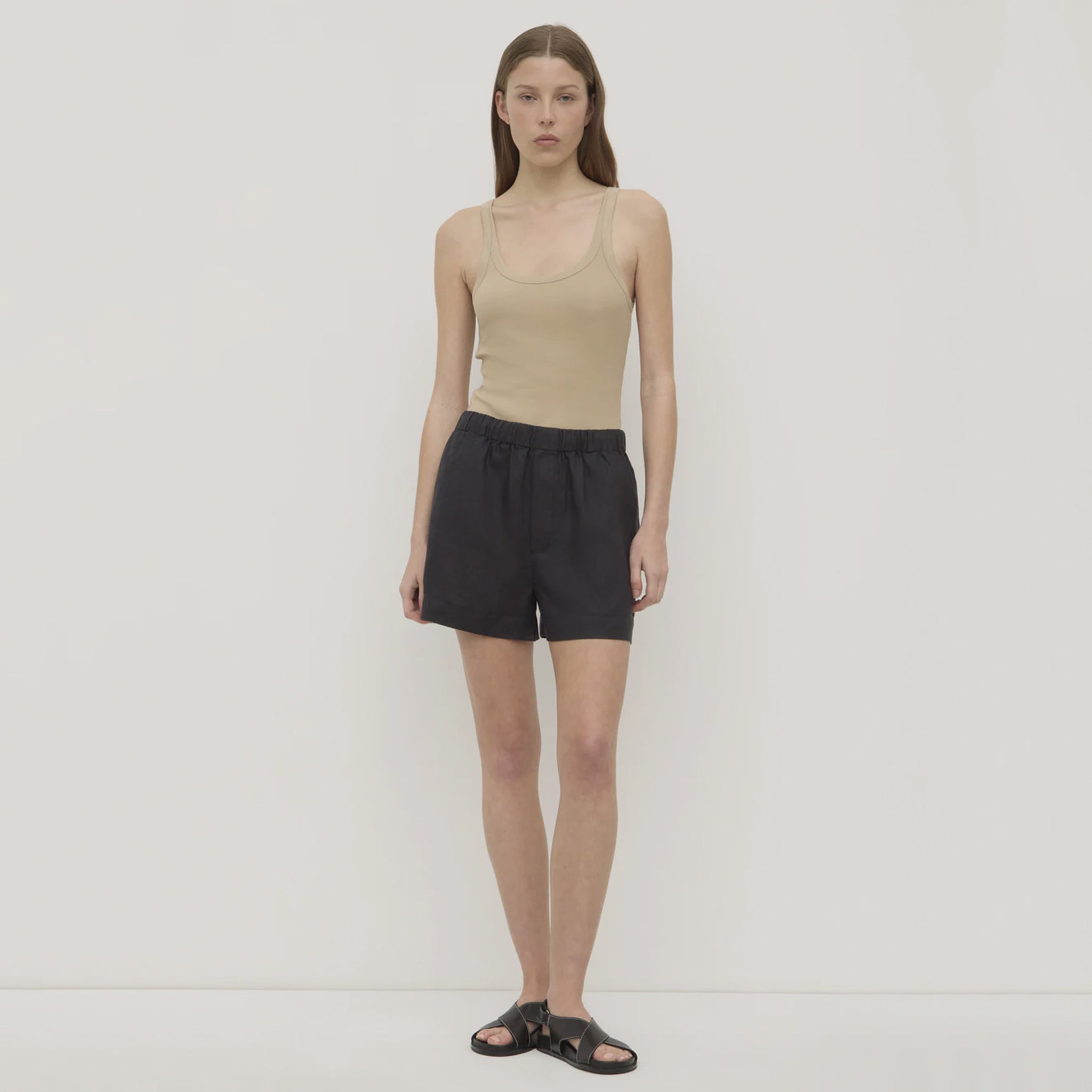 Woman wearing a beige tank top and black shorts on a plain background