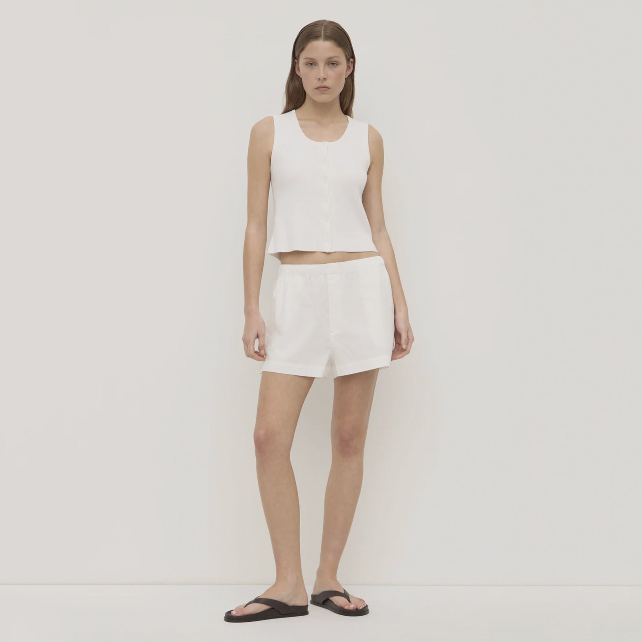 Woman wearing a white sleeveless top and skirt on a plain background