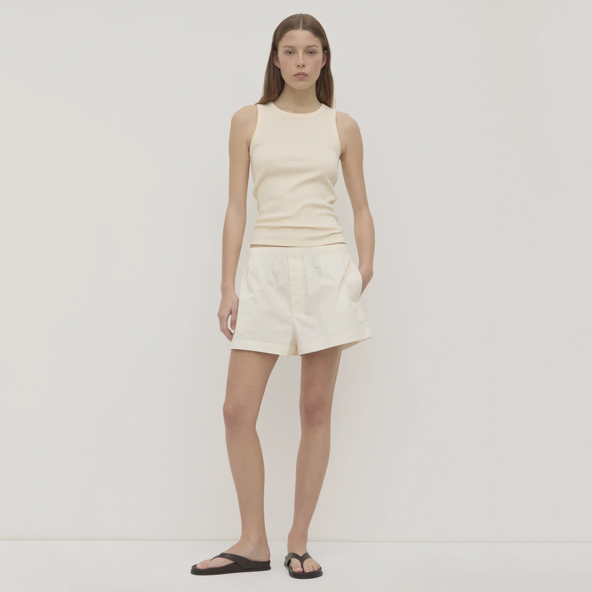 Woman wearing a beige sleeveless top and shorts on a white background