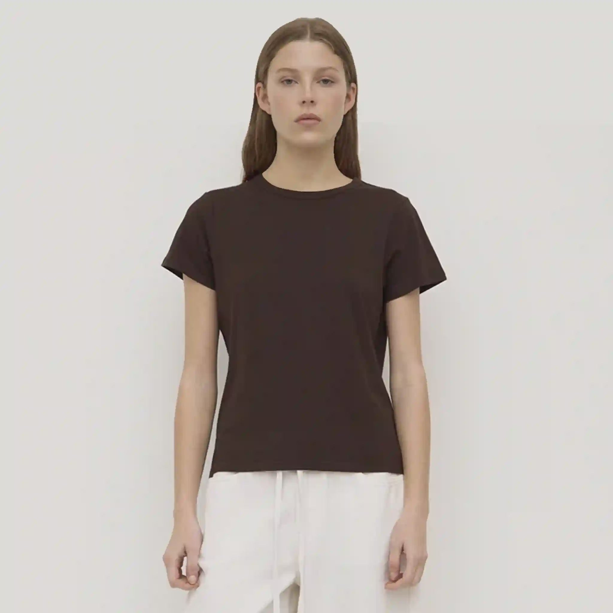 Person wearing a brown t-shirt and white pants against a plain background