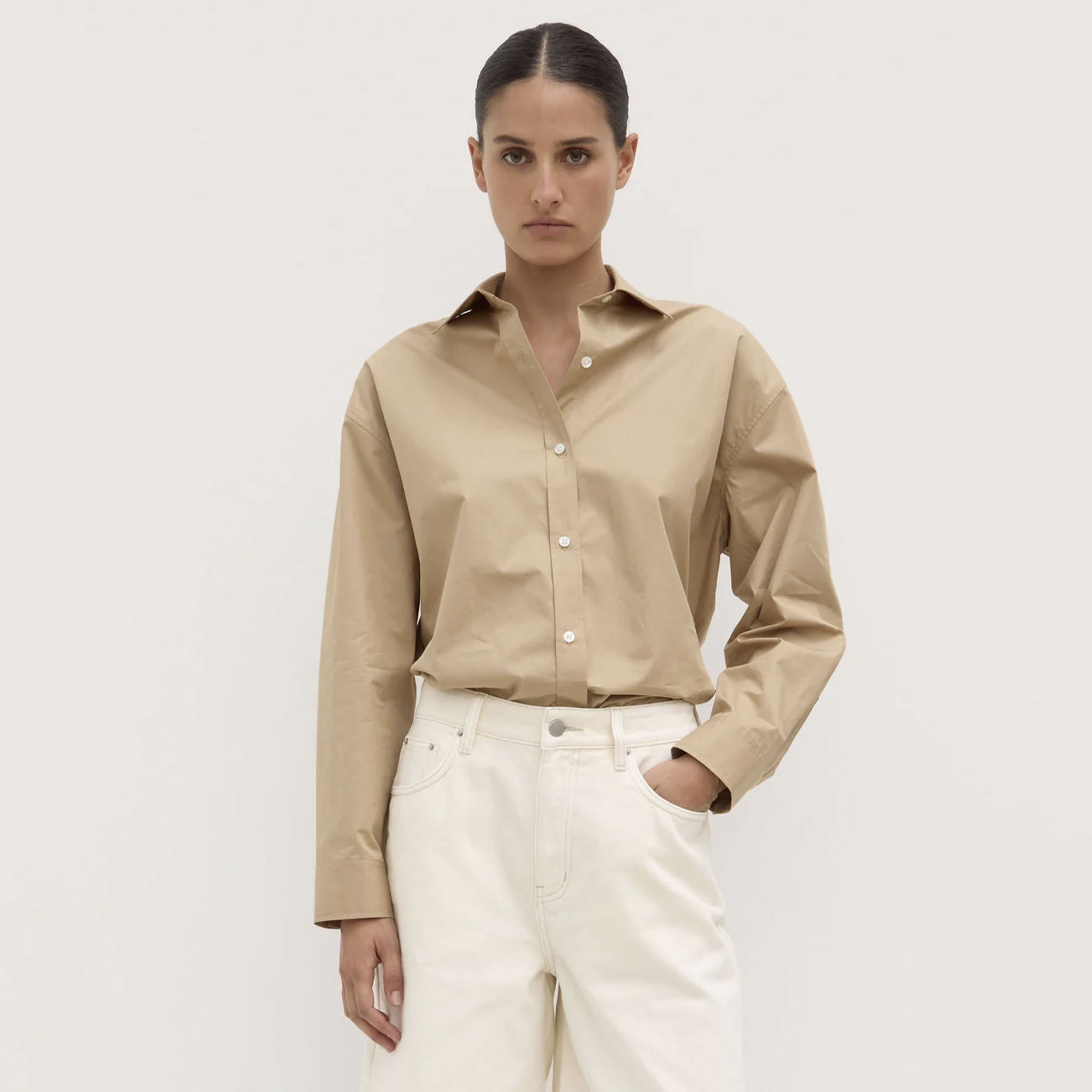 Woman wearing a beige shirt and white pants against a plain background