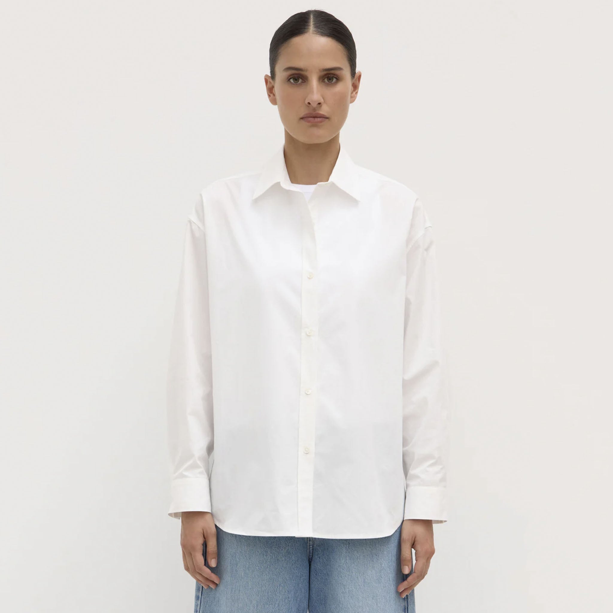 Person wearing a white shirt and blue jeans on a plain background