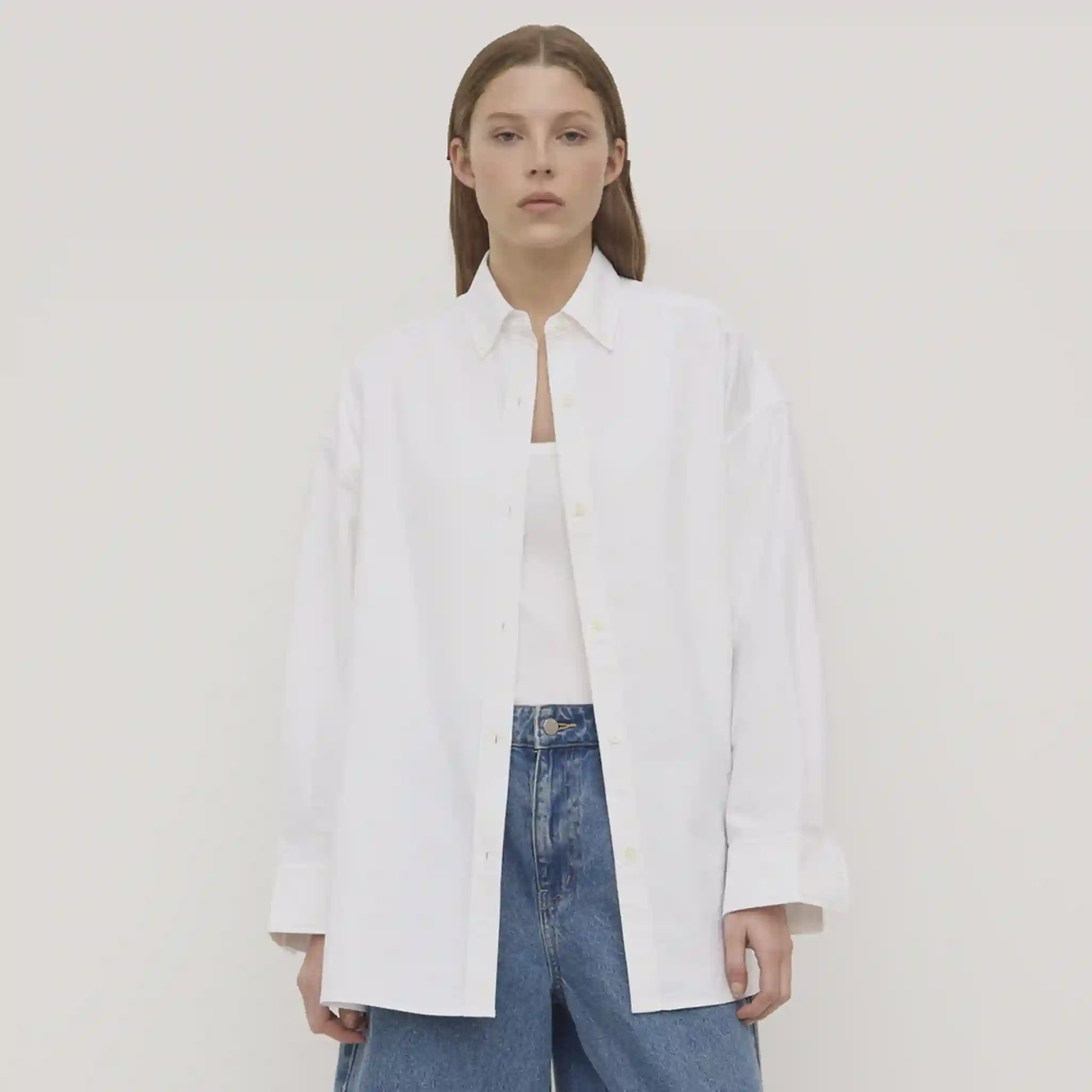 Person wearing a white shirt and blue jeans against a plain background