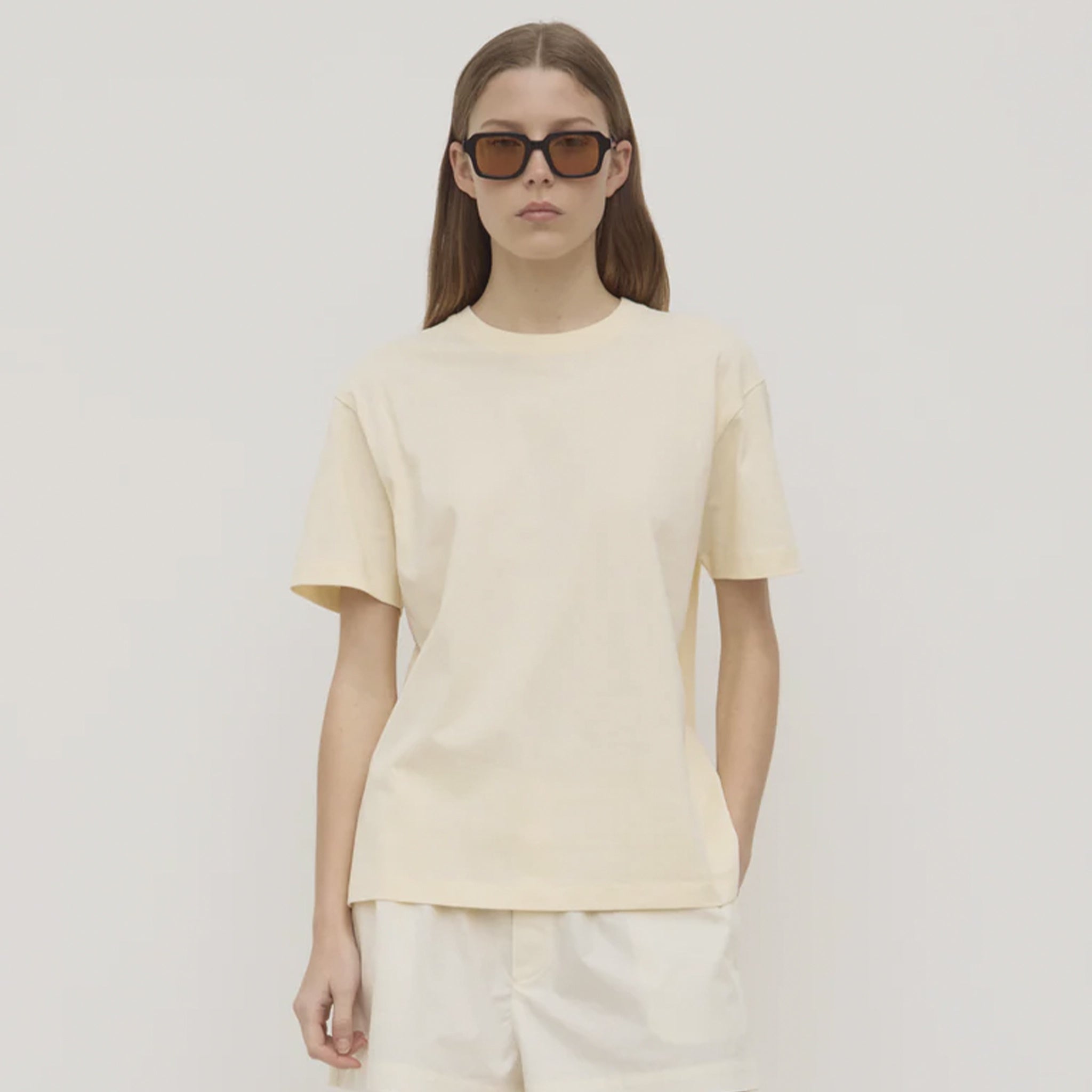 Person wearing a light yellow t-shirt and sunglasses on a plain background