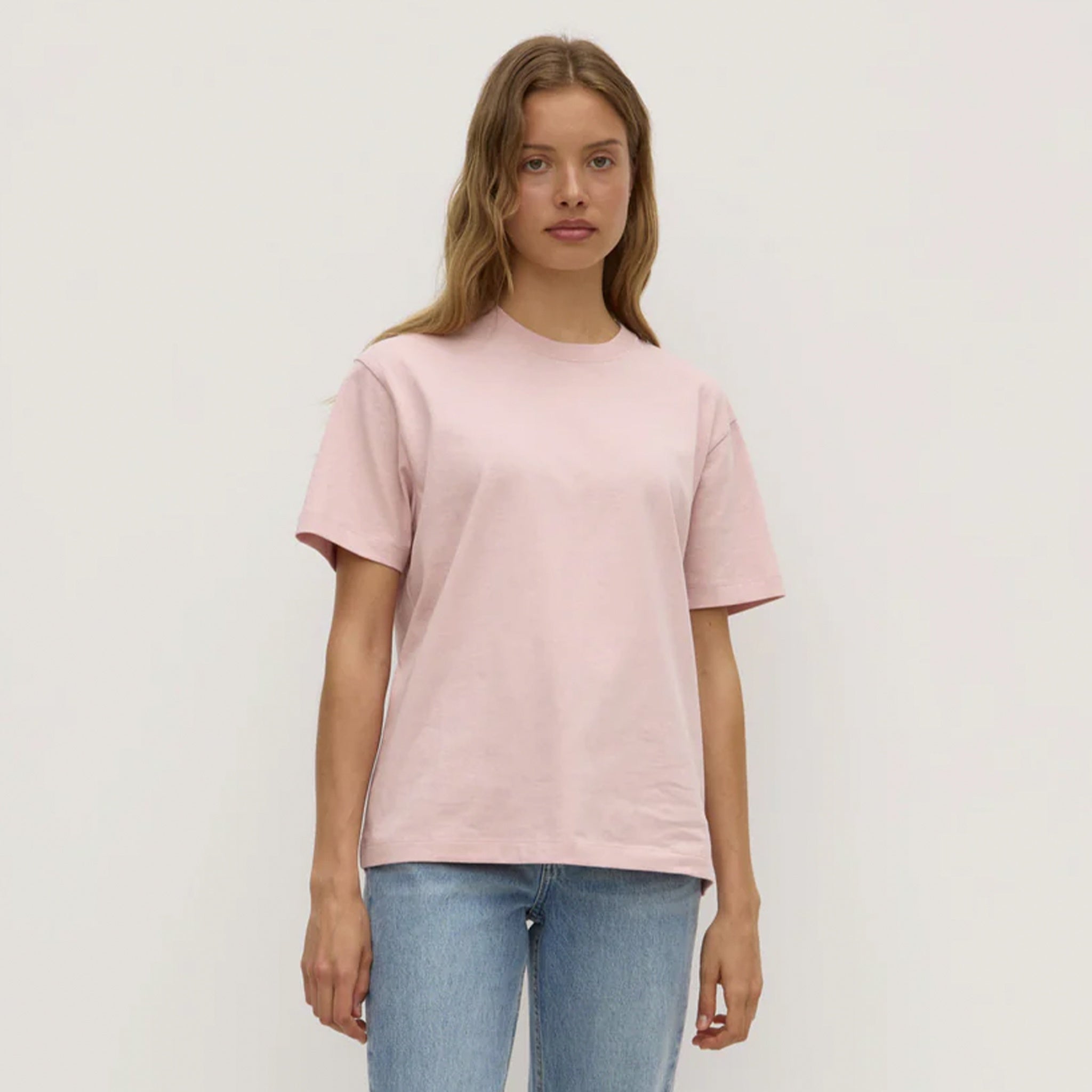 Person wearing a light pink t-shirt and blue jeans on a plain background