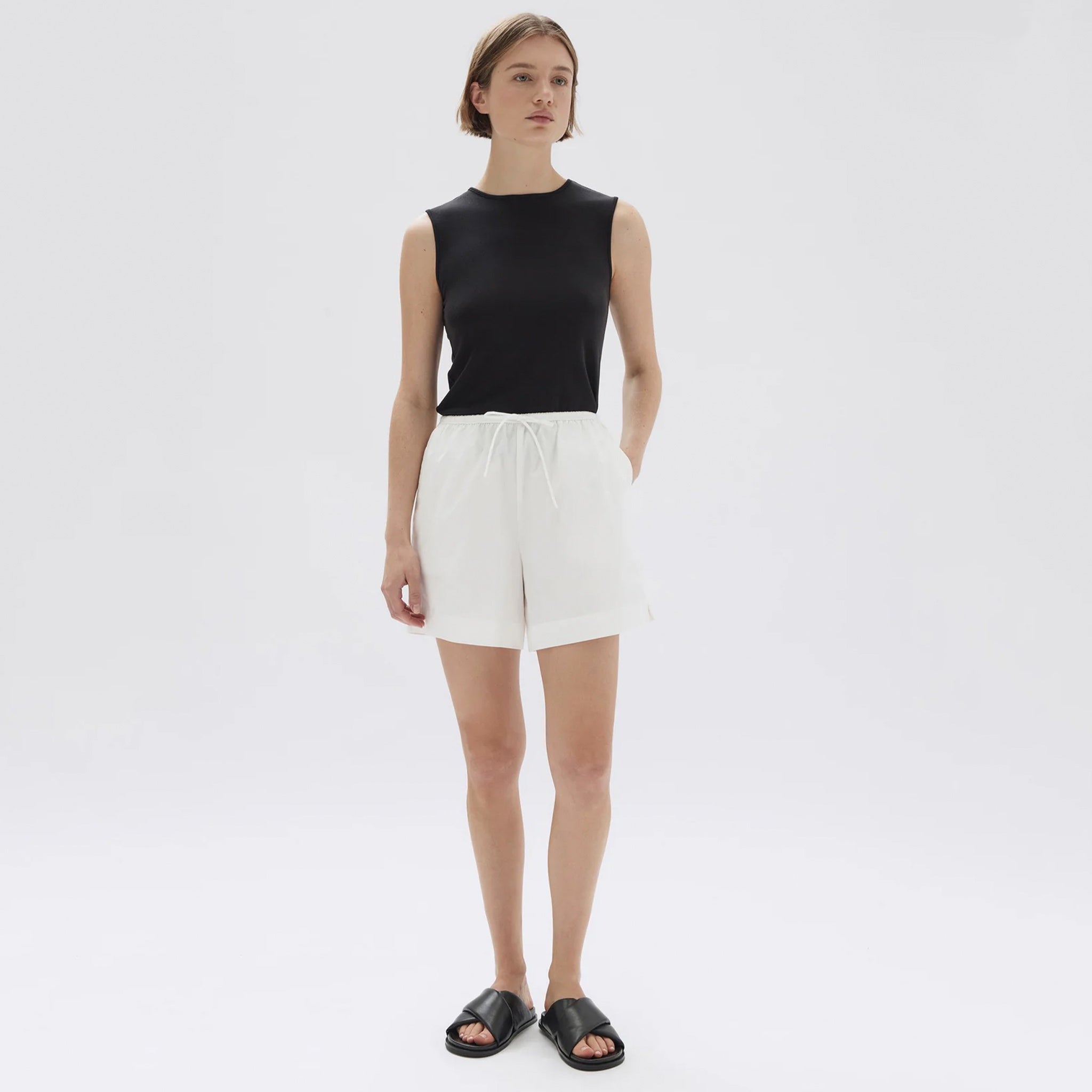 A model wearing white A-line poplin shorts with a tie front detail and elasticated waist, paired with a black sleeveless top.