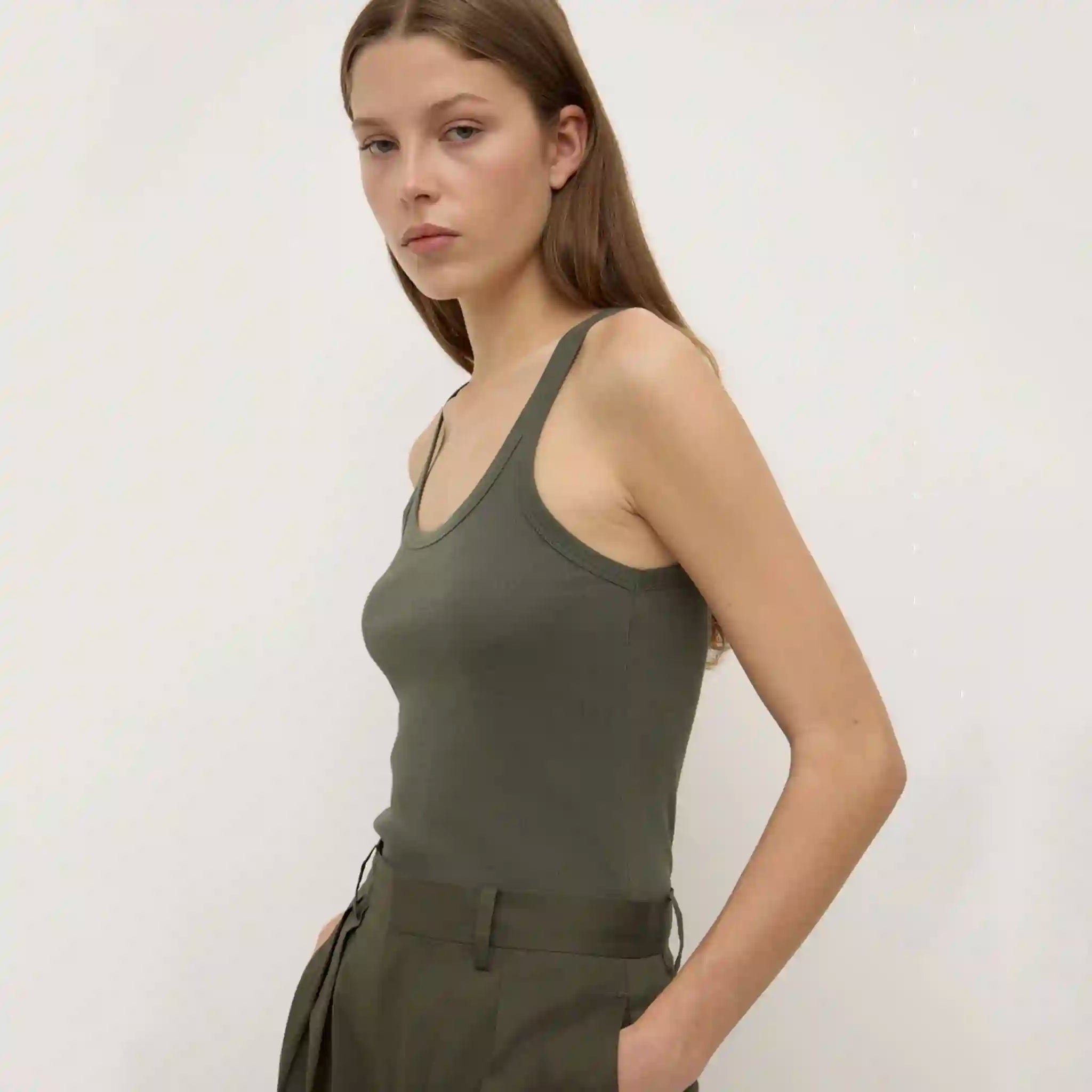 Woman wearing a green tank top and pants against a white background