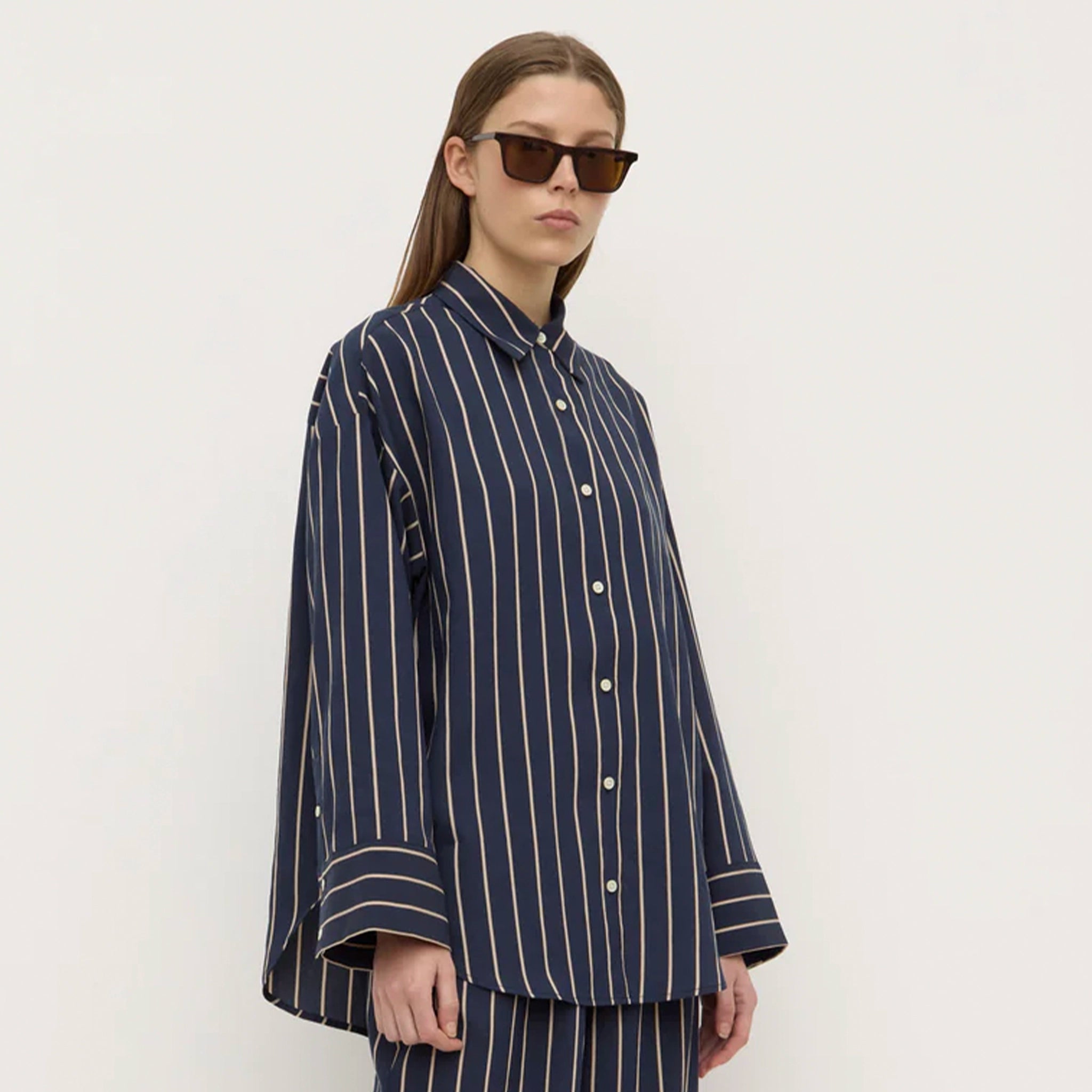 Person wearing a navy striped shirt and pants with sunglasses on a white background