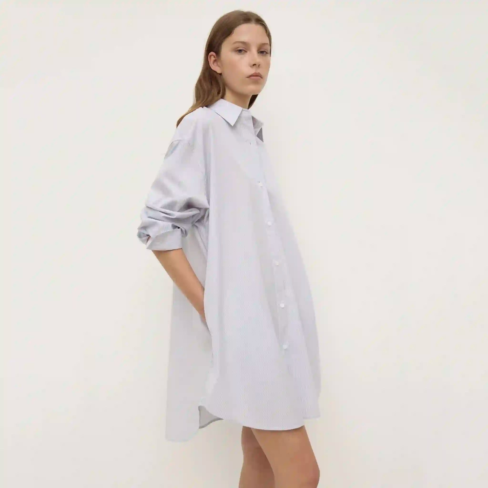 Woman wearing a light gray oversized shirt dress on a white background