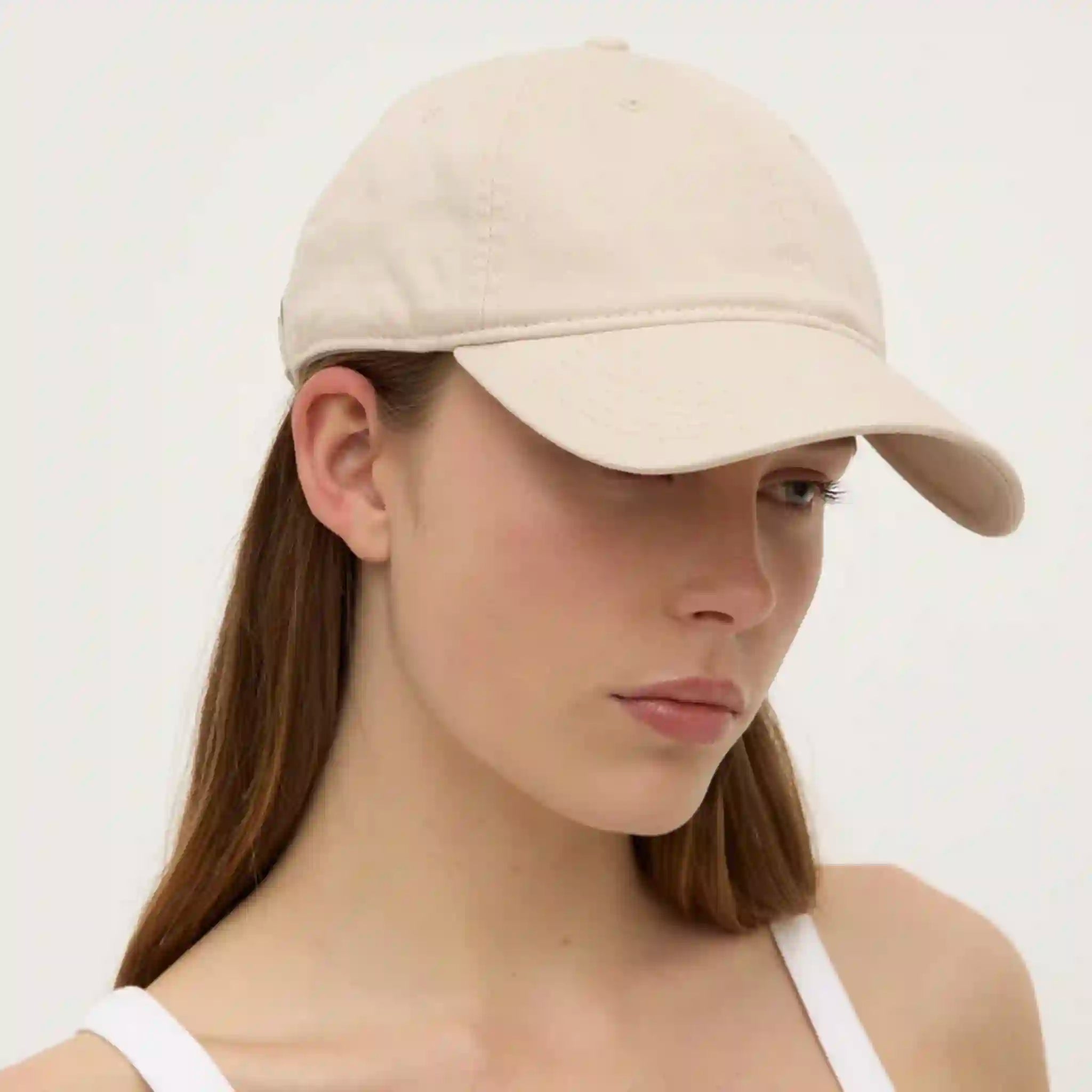 Woman wearing a beige baseball cap against a plain background