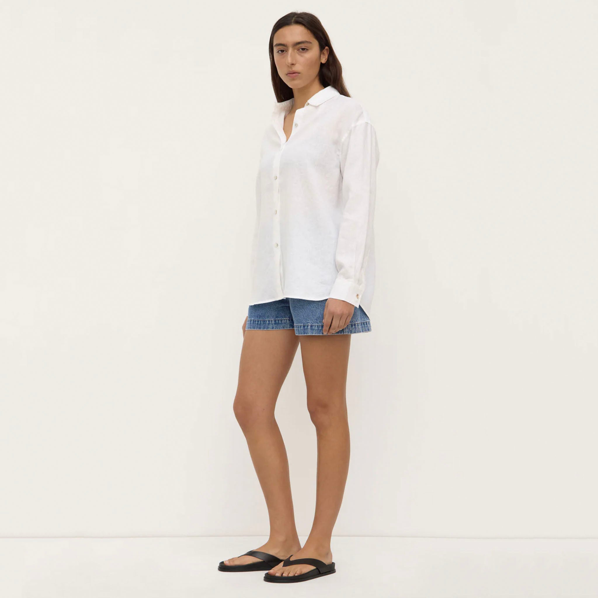 Woman wearing a white shirt and denim shorts on a plain background