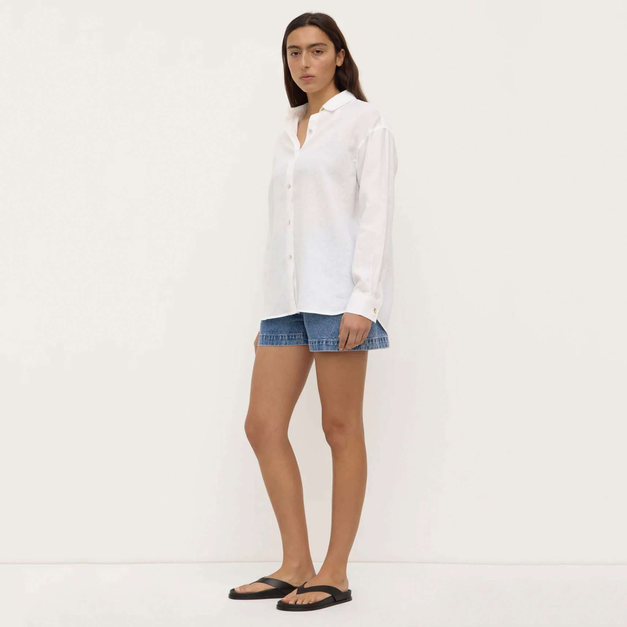 Woman wearing a white shirt and denim shorts on a plain background