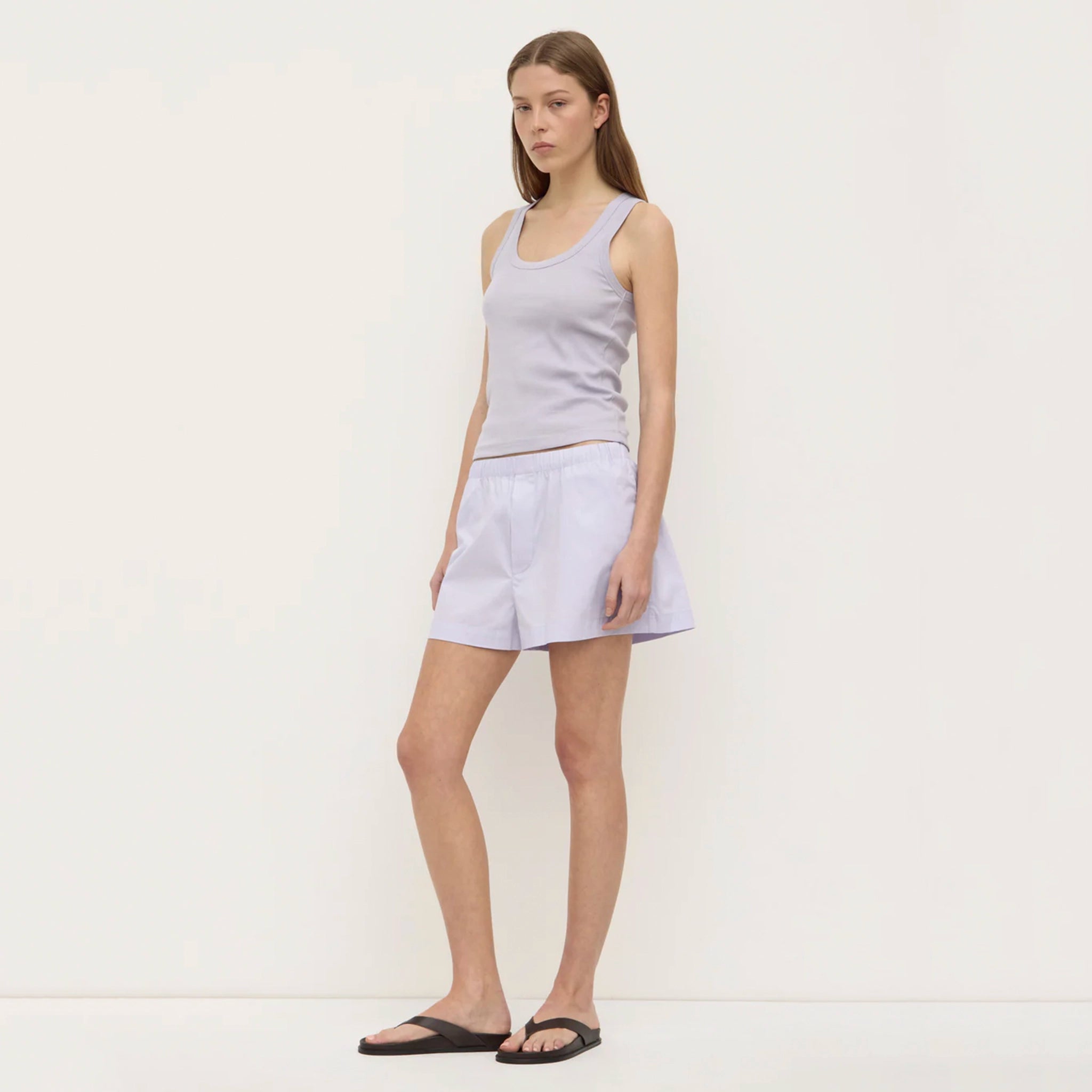 Woman wearing a light gray tank top and shorts on a white background