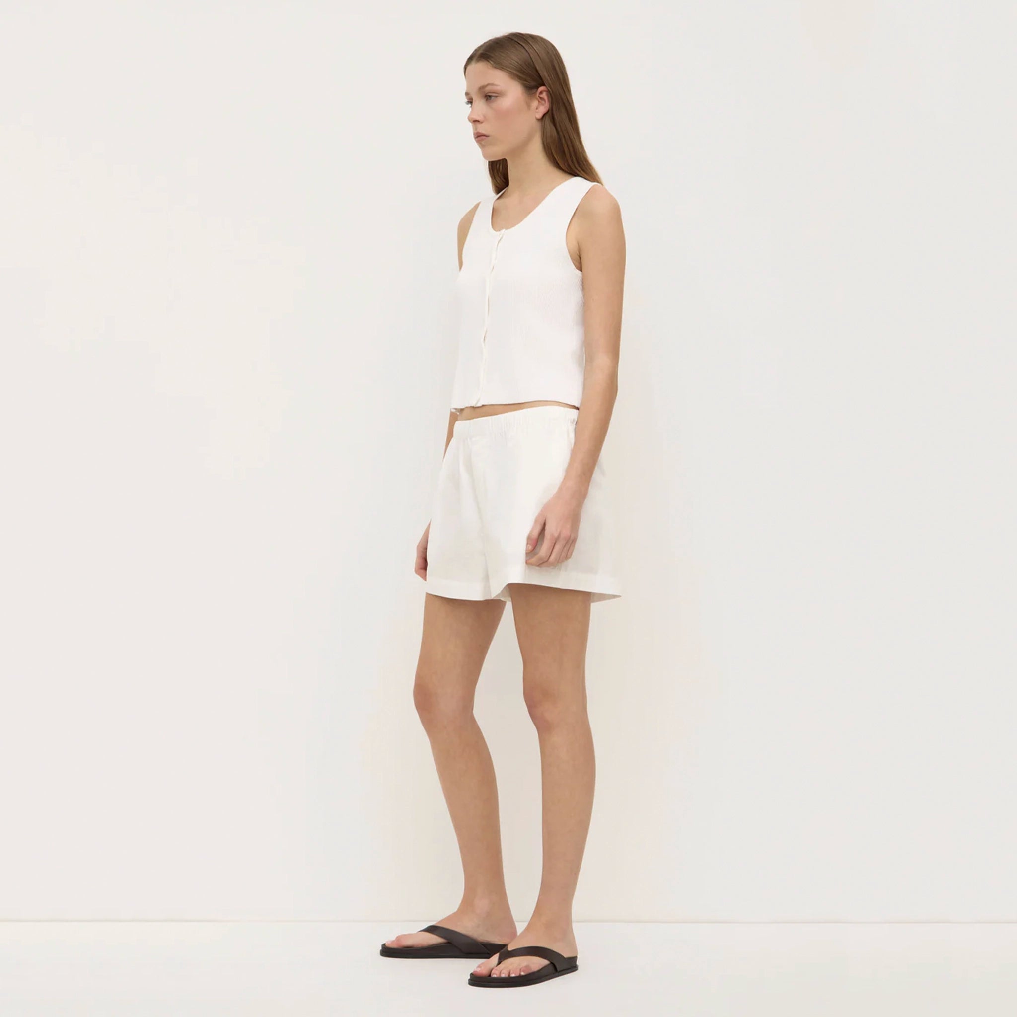 Woman wearing a white sleeveless top and shorts on a plain background