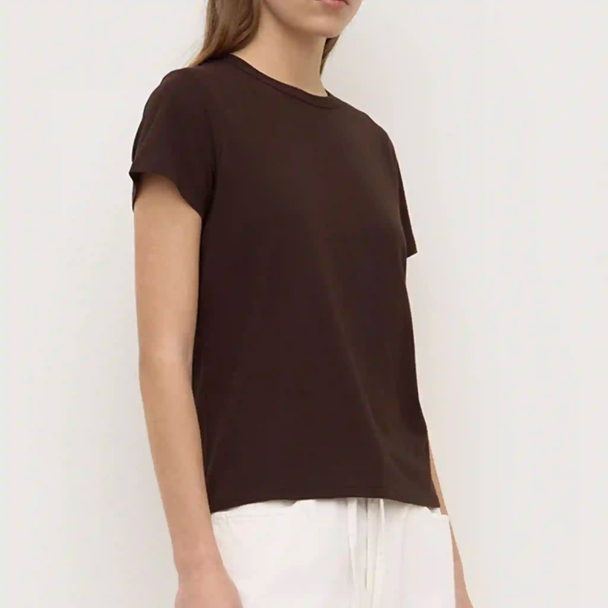 Person wearing a brown t-shirt and white pants against a plain background