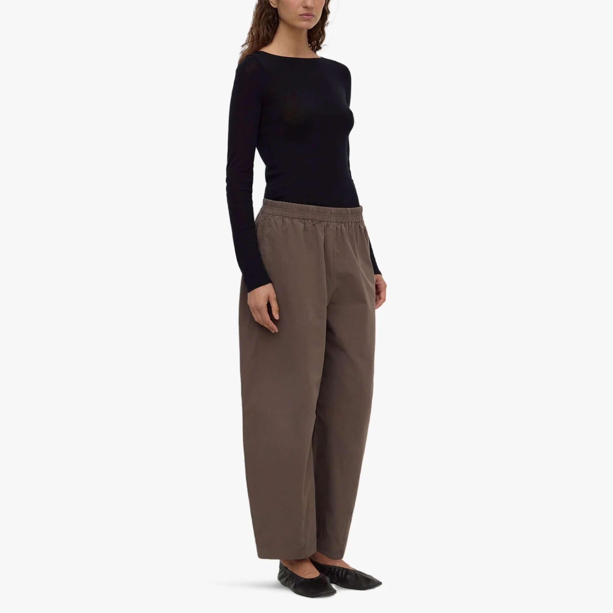 Model wearing Assembly Label barrel pants in bark with a black long-sleeve top and flat shoes.
