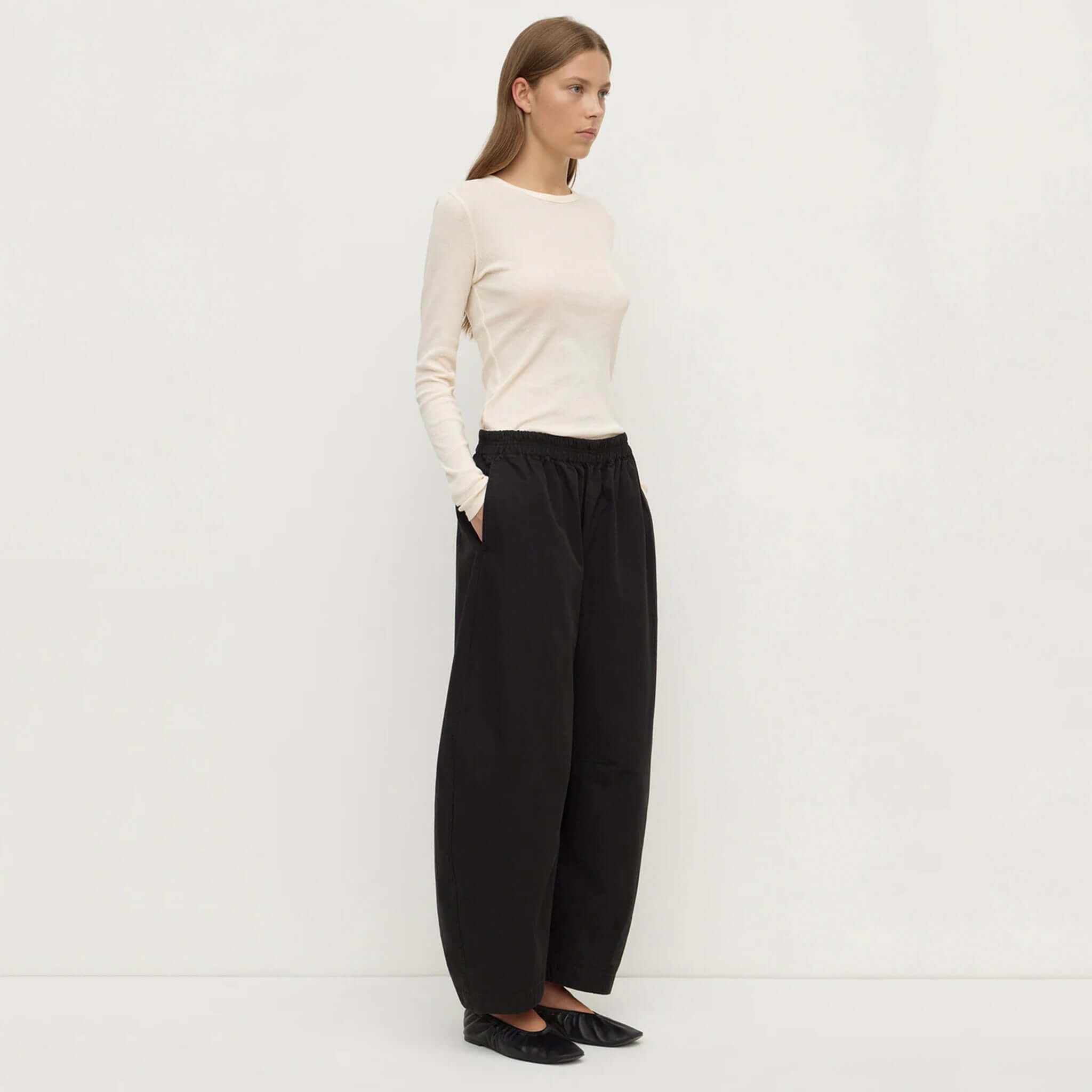 Model wearing Assembly Label Lola Barrel Pants - Black with a cream long-sleeve top and black shoes.