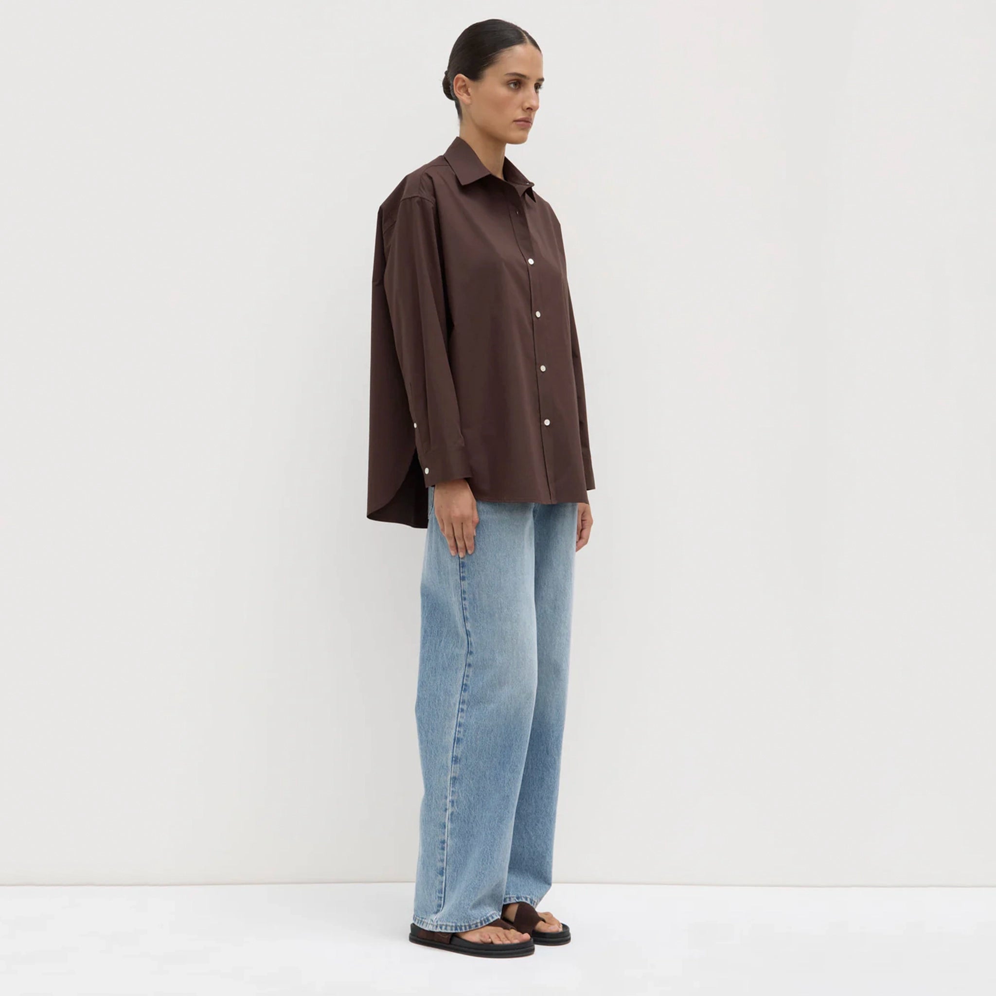 Person wearing a brown shirt and blue jeans against a white background