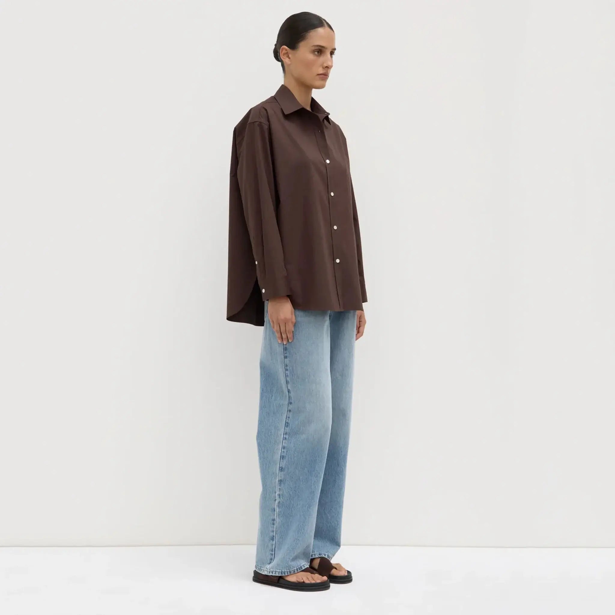 Person wearing a brown shirt and blue jeans against a white background