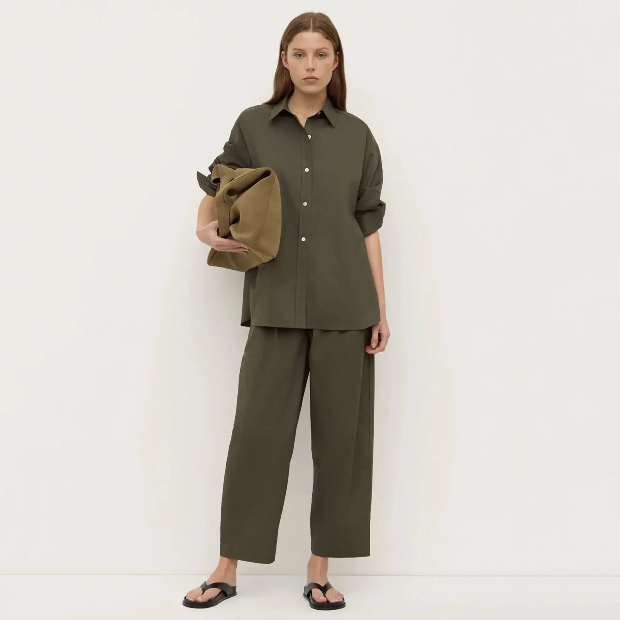 Woman wearing an olive green outfit holding a jacket against a white background
