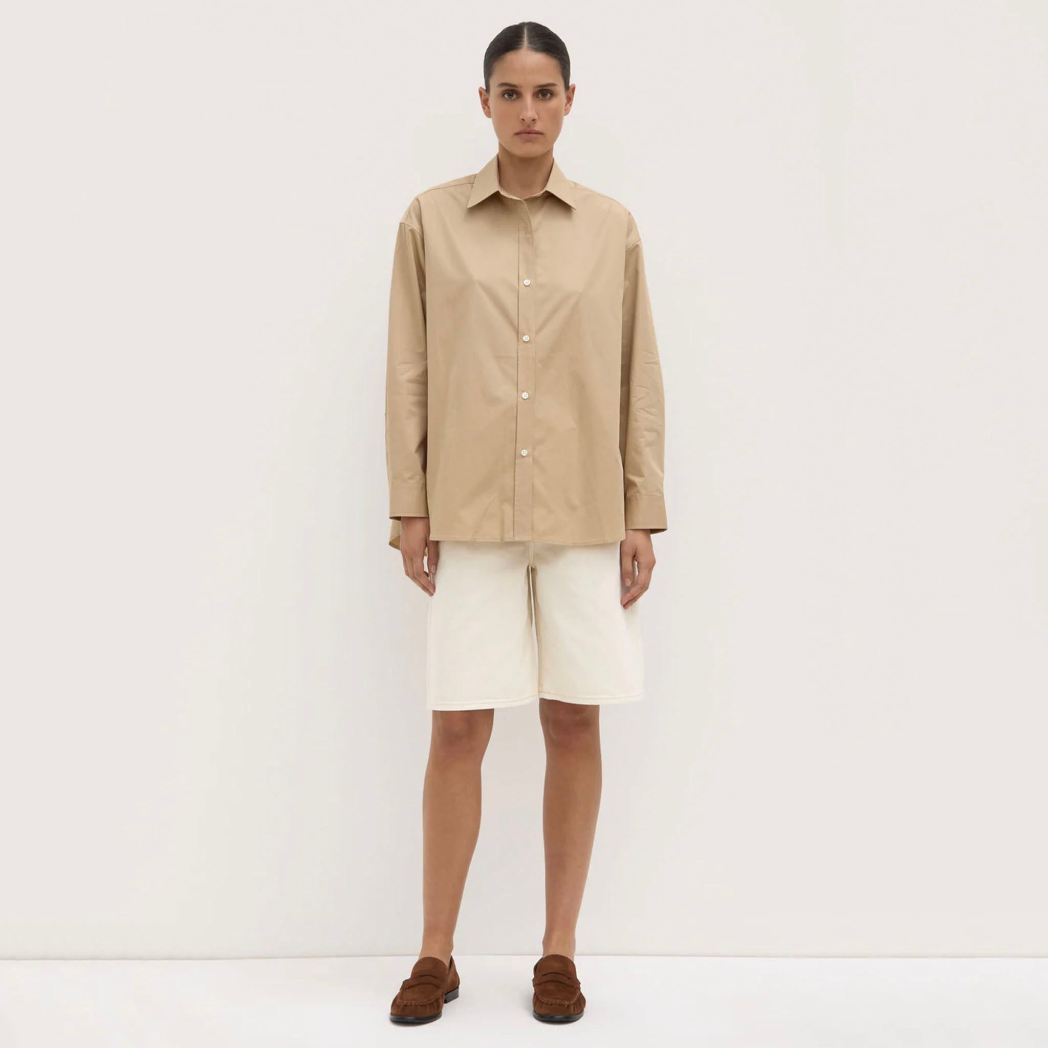 Person wearing a beige shirt and white pants on a white background