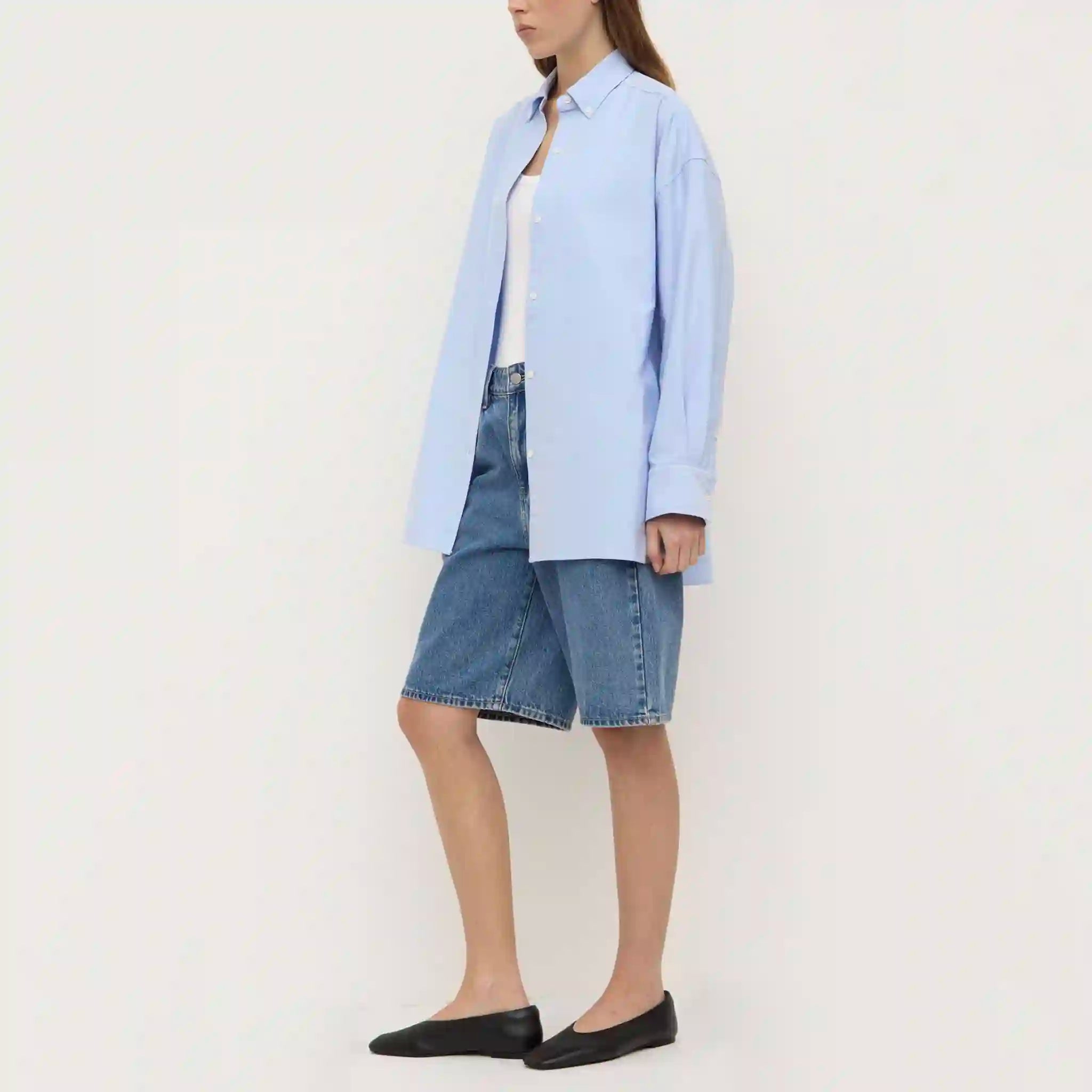 Person wearing a light blue shirt and denim skirt on a white background
