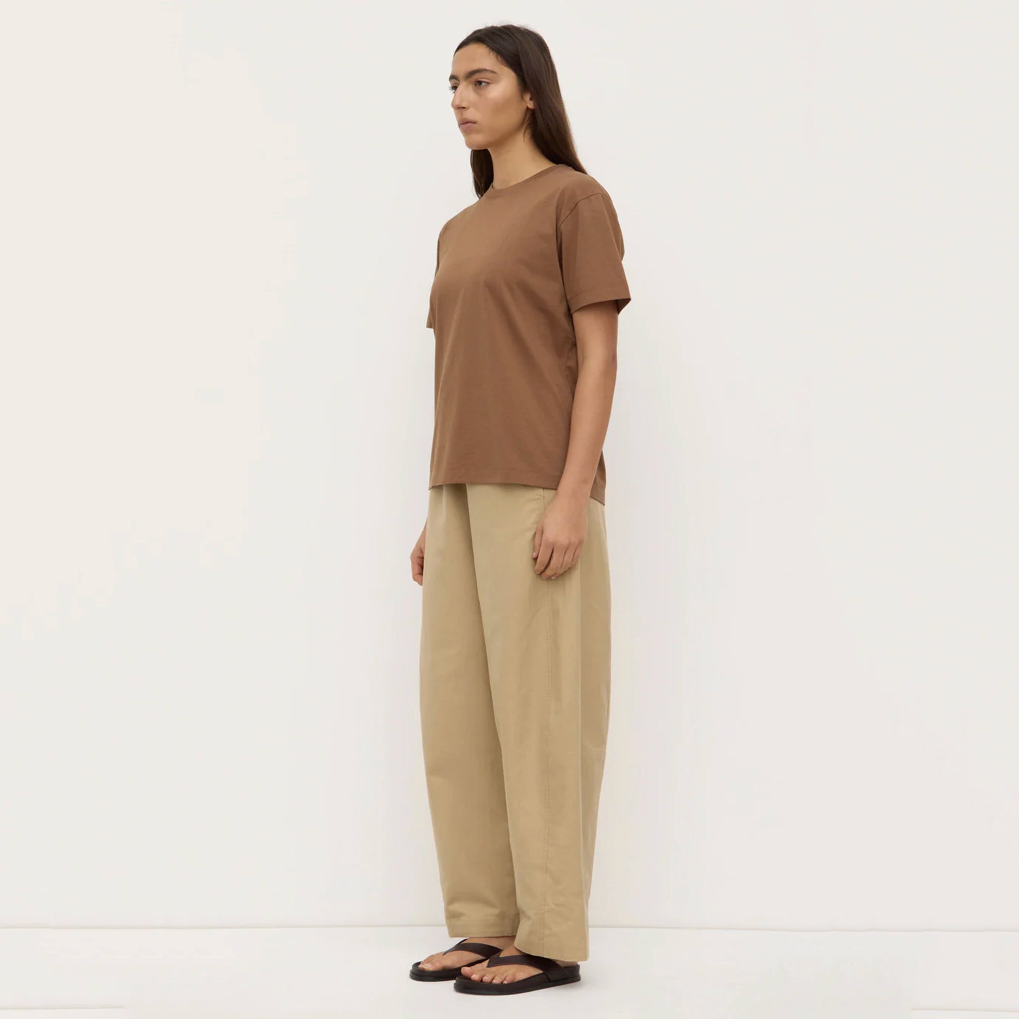 Woman wearing a brown t-shirt and beige pants on a white background