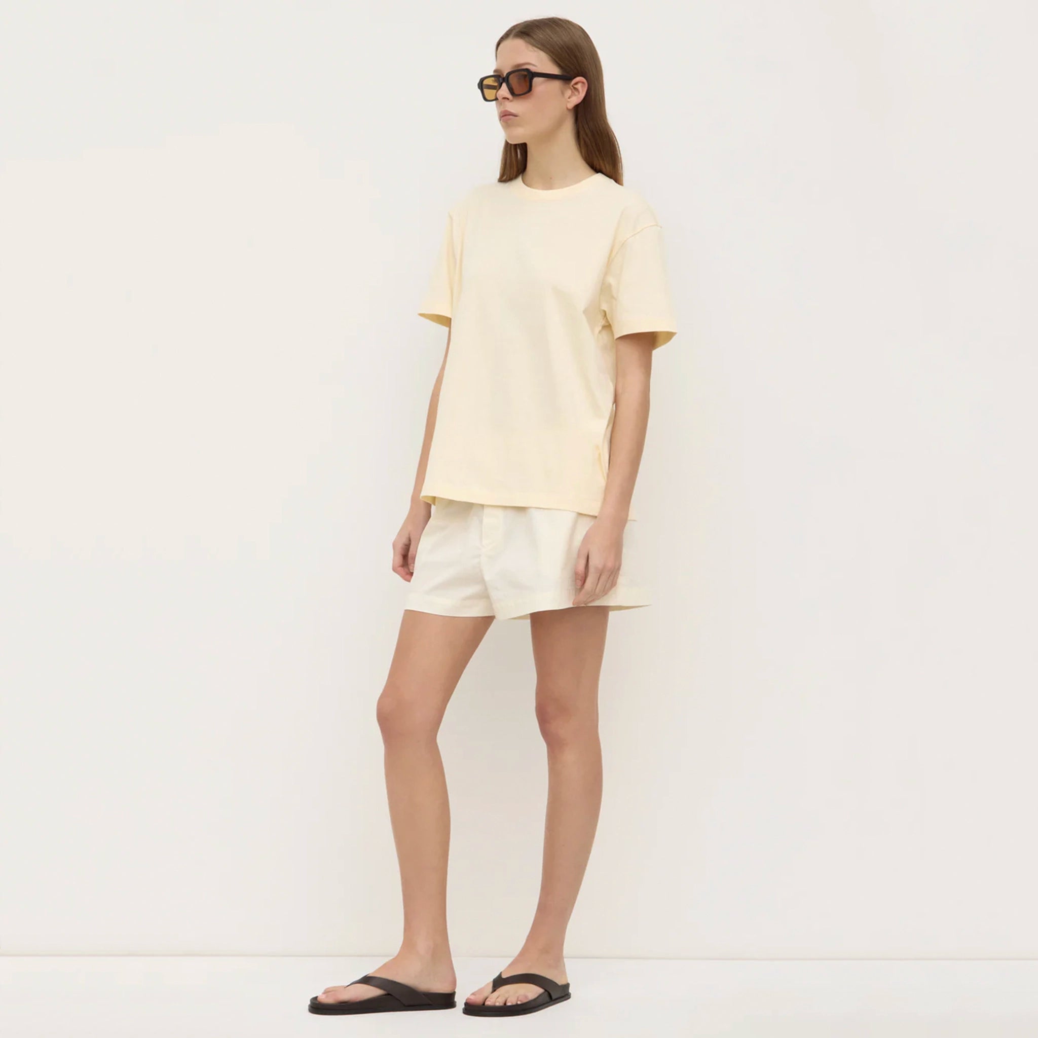 Woman wearing a light yellow top and shorts with black sandals on a white background