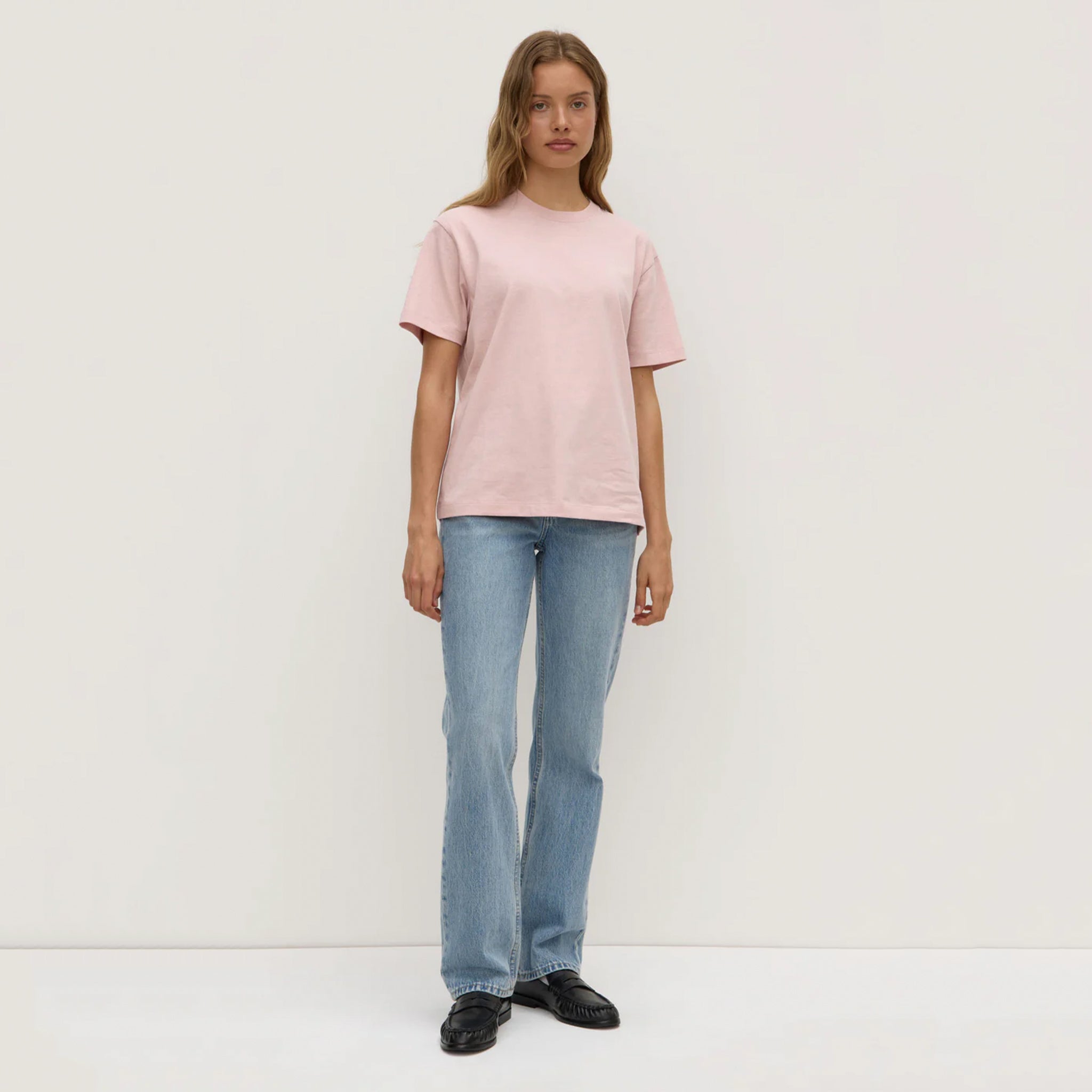 Person wearing a pink t-shirt and light blue jeans on a white background