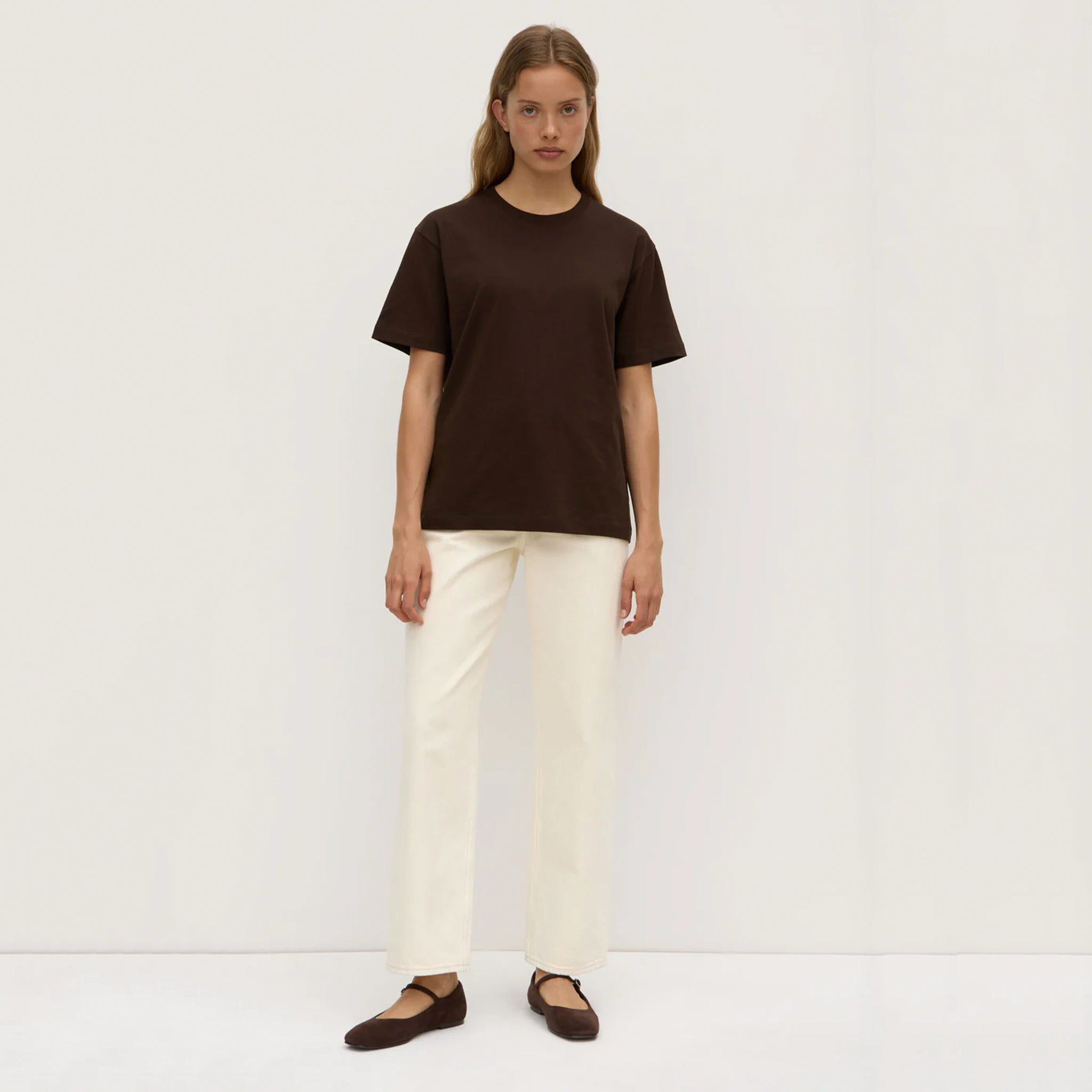 Person wearing a brown t-shirt and white pants on a white background