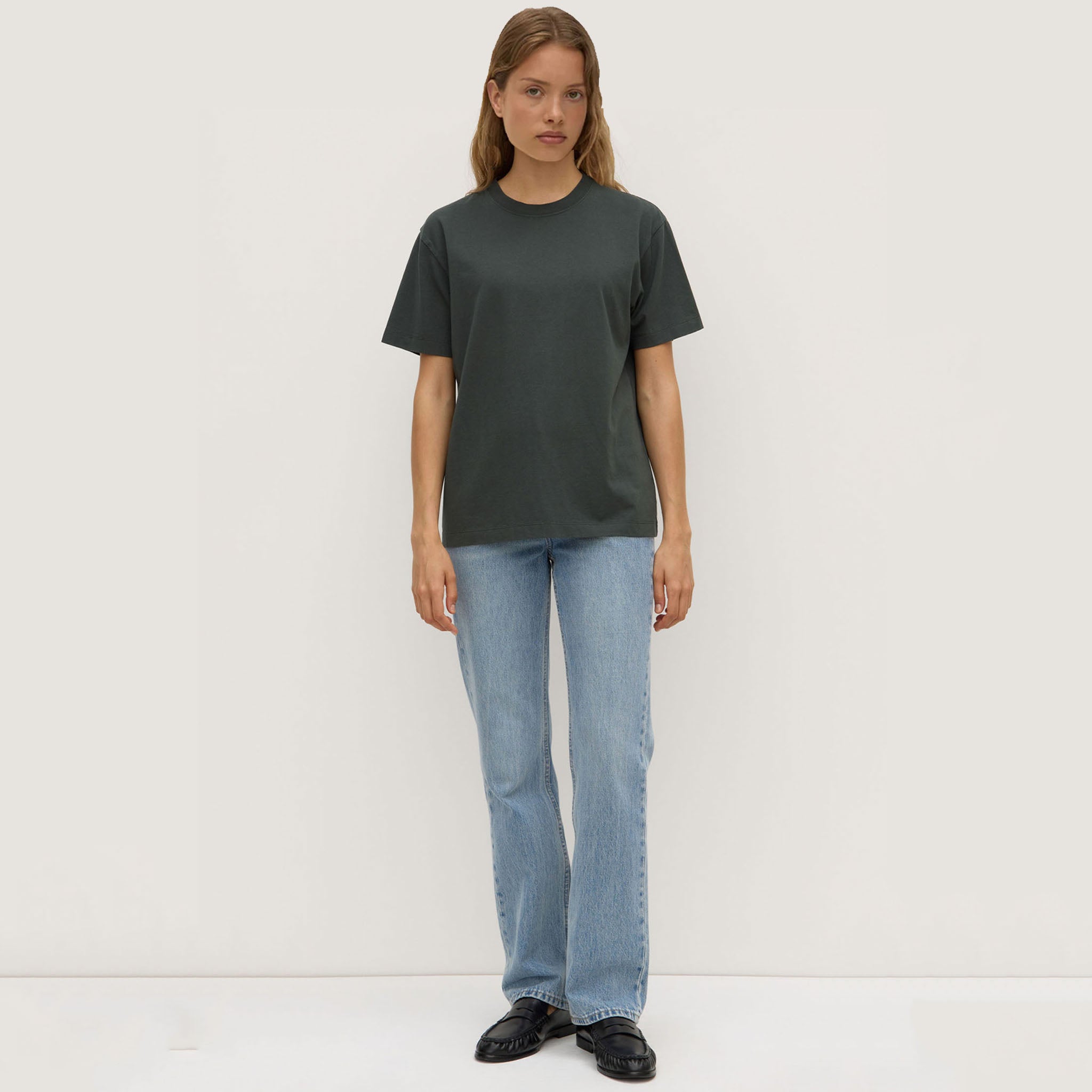 Person wearing a dark green t-shirt and light blue jeans on a white background