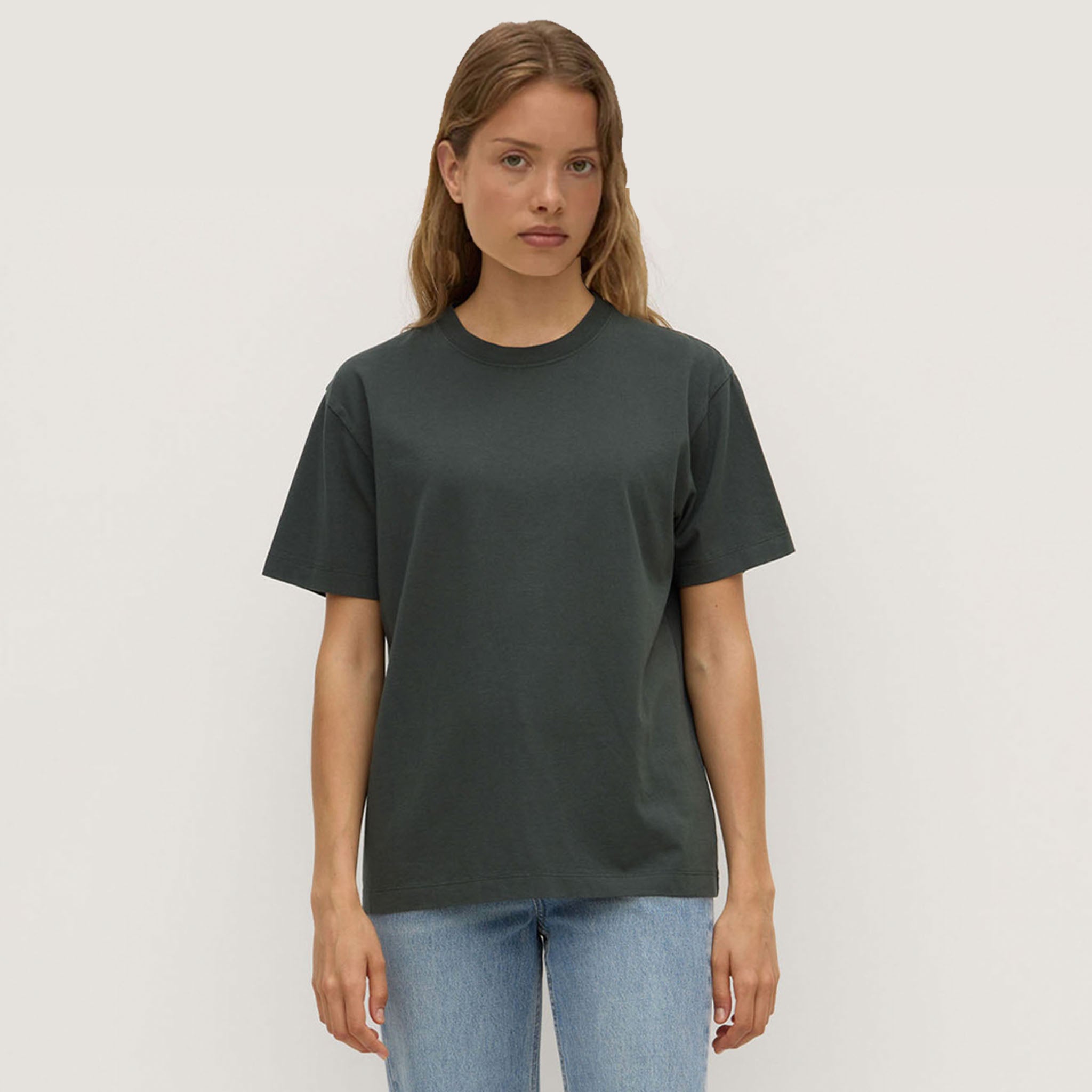 Woman wearing a dark green t-shirt and light blue jeans against a plain background