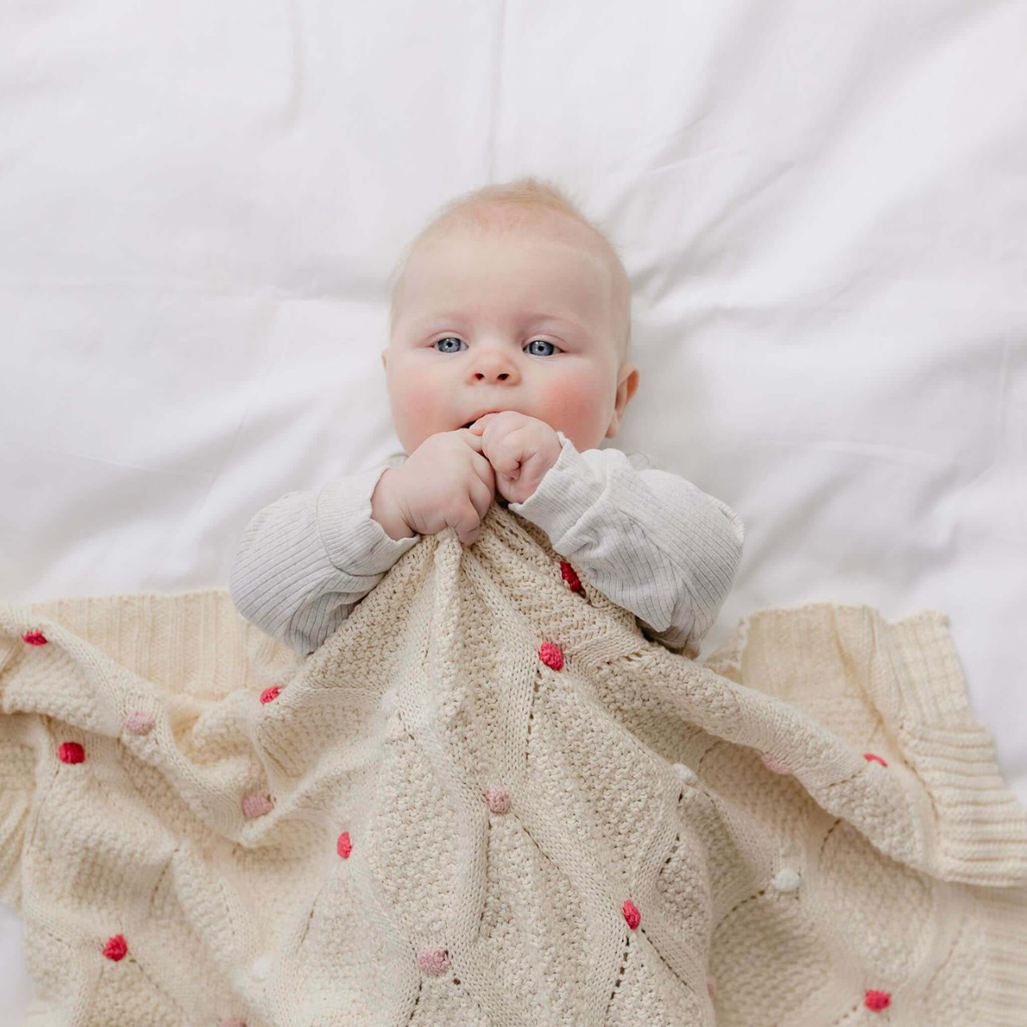 Baby Cotton Lucy Blanket - Ivory & Pink being used by a baby, showcasing its soft texture and color.