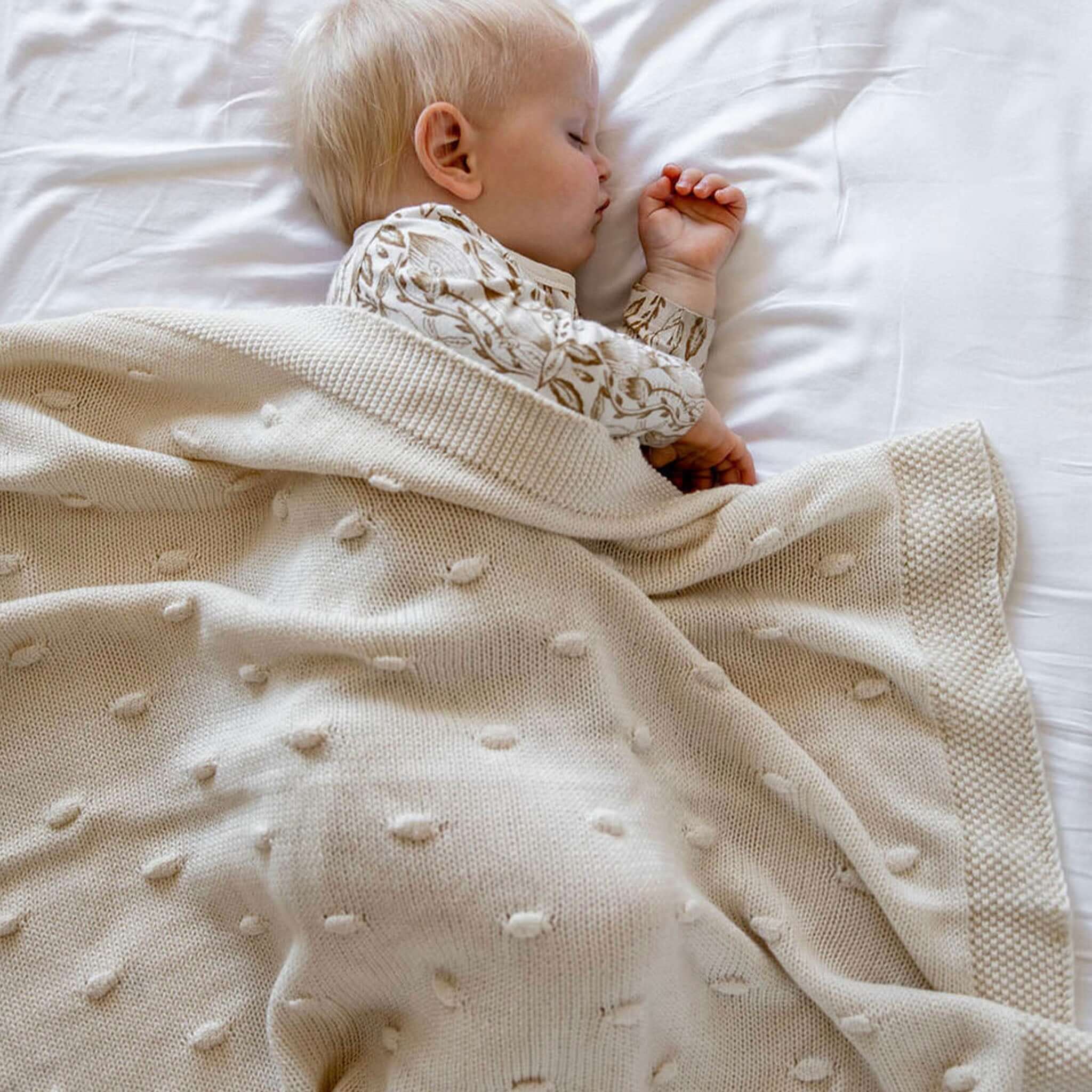 Baby Cotton Marshmallow Blanket - Natural draped over a sleeping infant on a bed, showcasing its soft texture and creamy color.