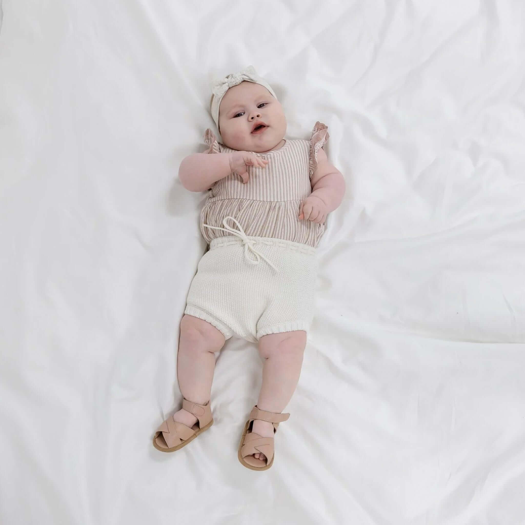 Baby Cotton Noah Bloomer - Ivory worn by an adorable baby on a white blanket, showcasing its soft and breathable design.